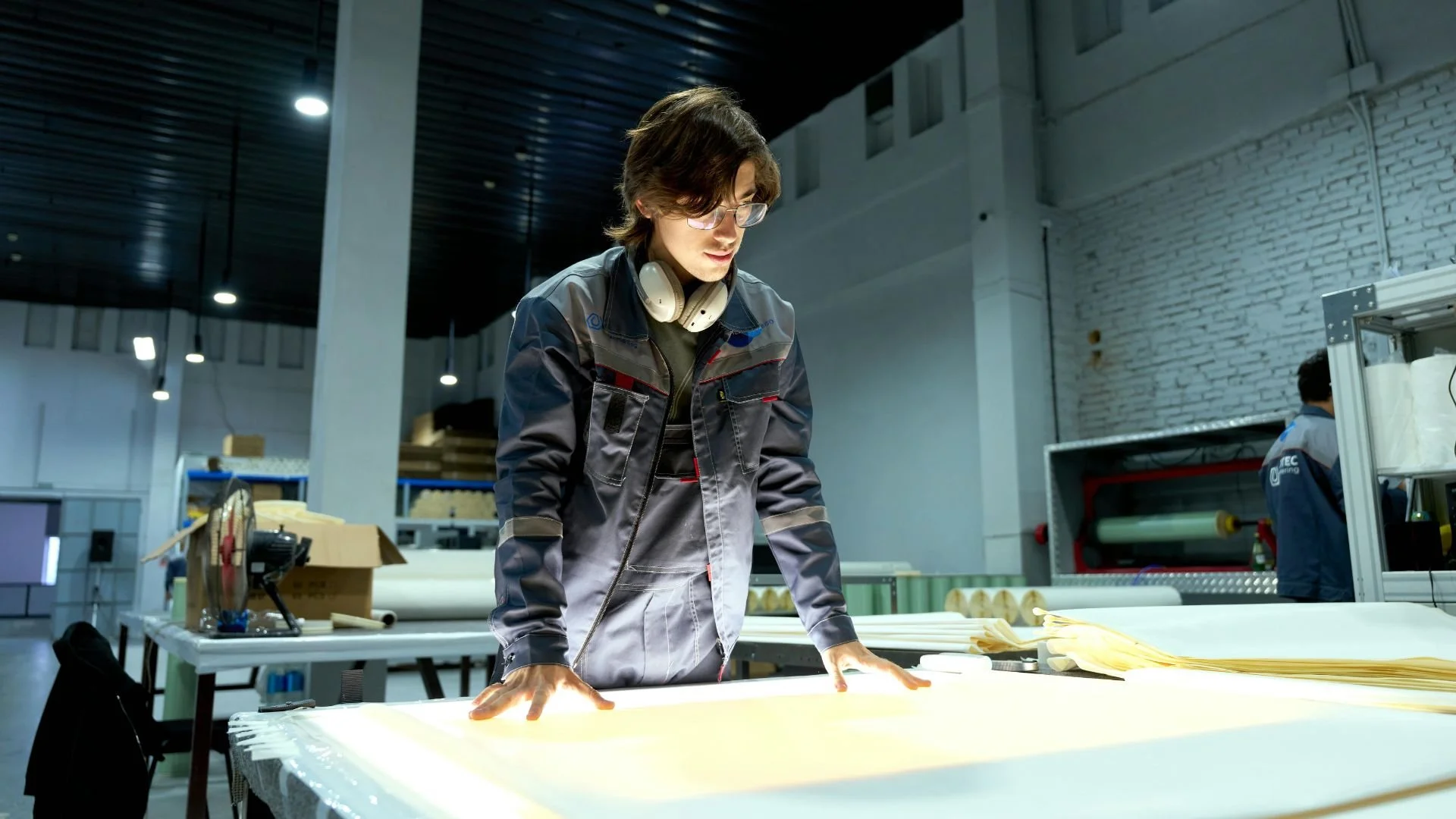 A person wearing workwear is looking at technical drawings in a production facility