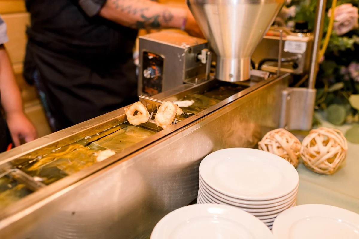 Deep fryer with onion rings being fried, plates stacked nearby, and decorative wicker balls on a counter.