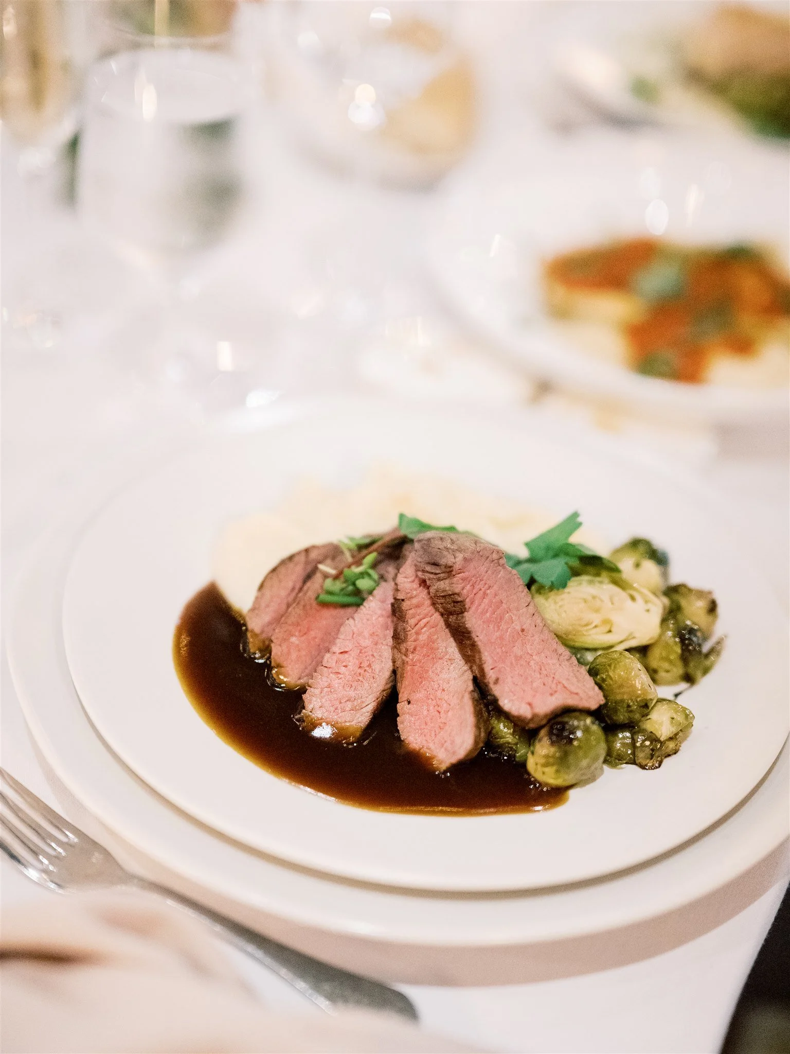 Sliced medium-rare beef served with green peas, sauce, and garnished with herbs on a white plate.