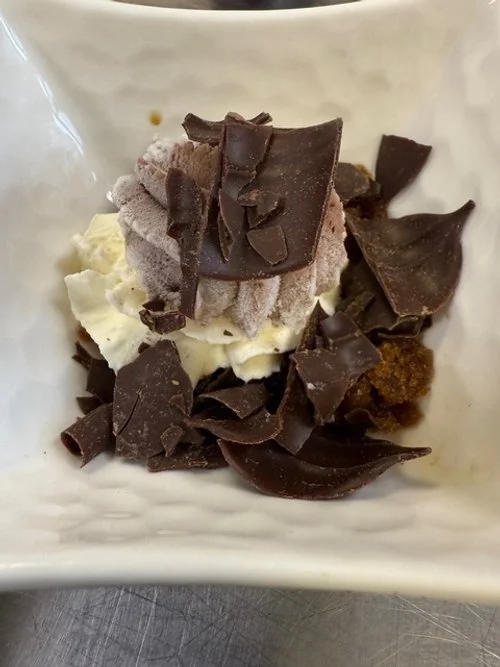A bowl of vanilla and chocolate ice cream topped with chocolate shavings and chunks.