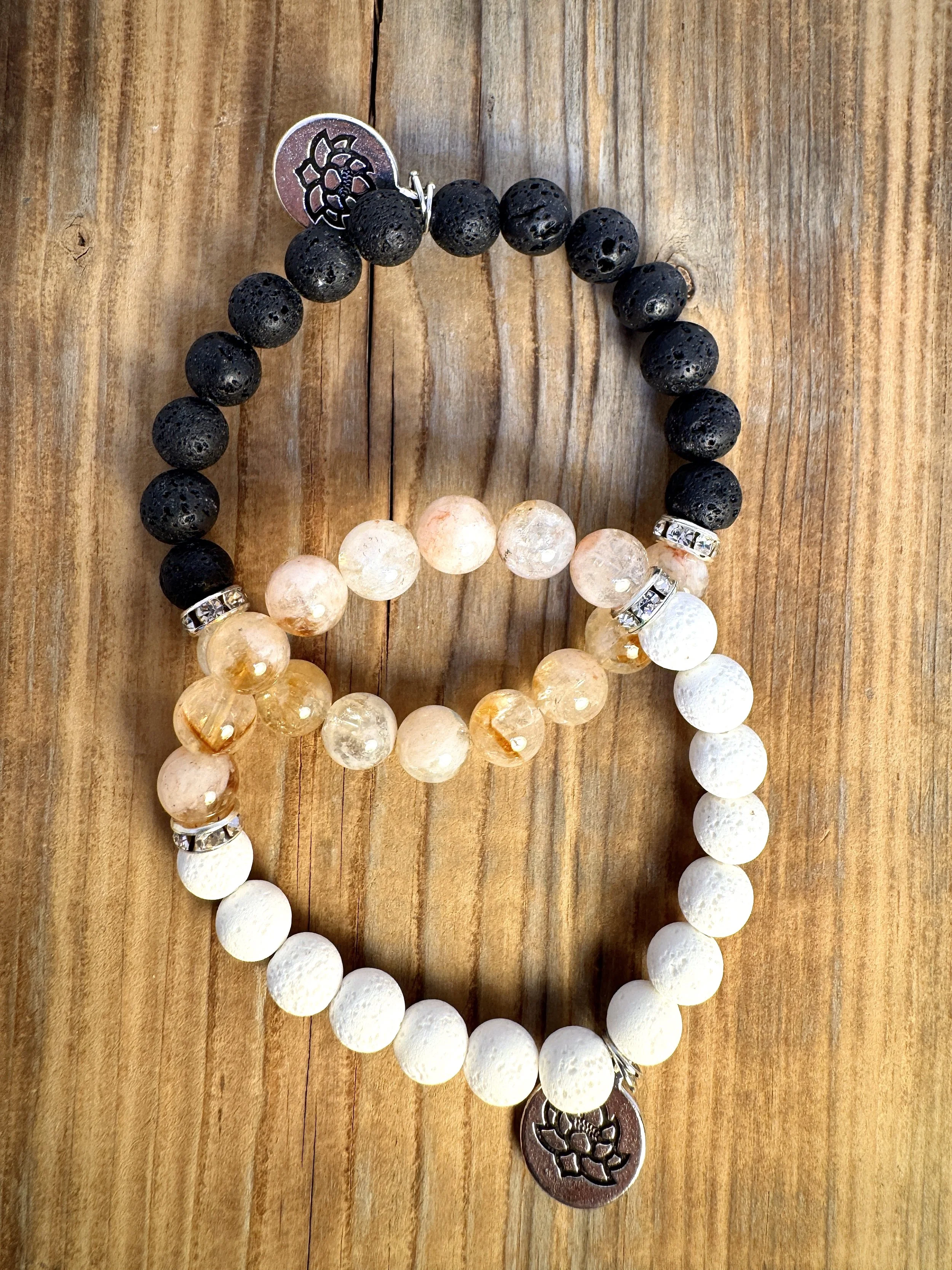 Three beaded bracelets on a wooden surface. The first is black with silver accents, the second is white with silver accents, and the third is beige with a silver charm.