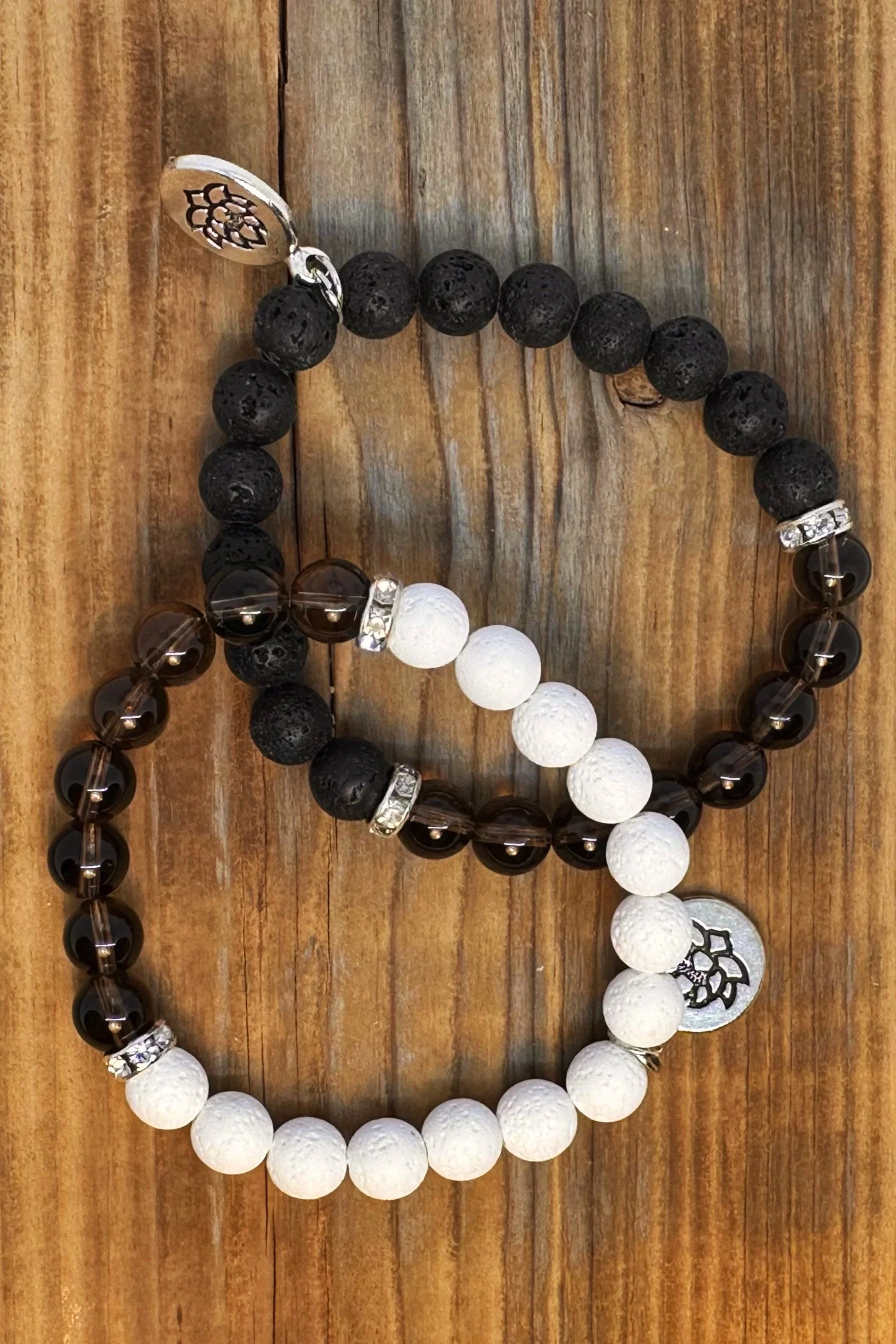 Two beaded bracelets with black and white beads, metal charms, and decorative spacers placed on a wooden surface.