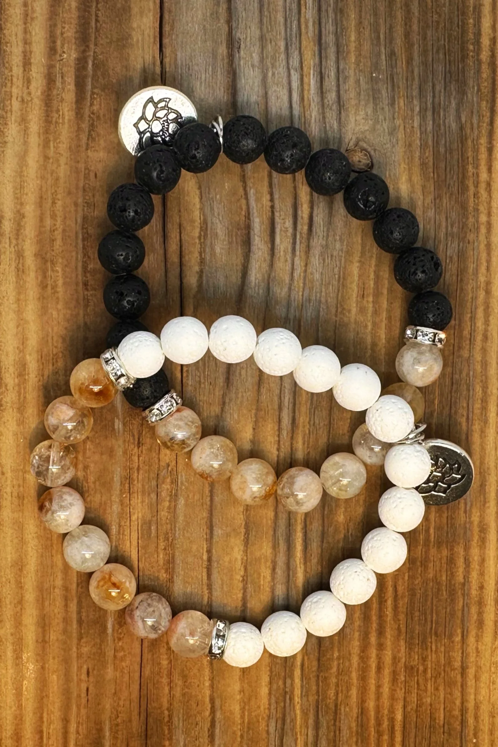 Three beaded bracelets on a wooden surface. The first is black with silver accents, the second is white with silver accents, and the third is beige with a silver charm.