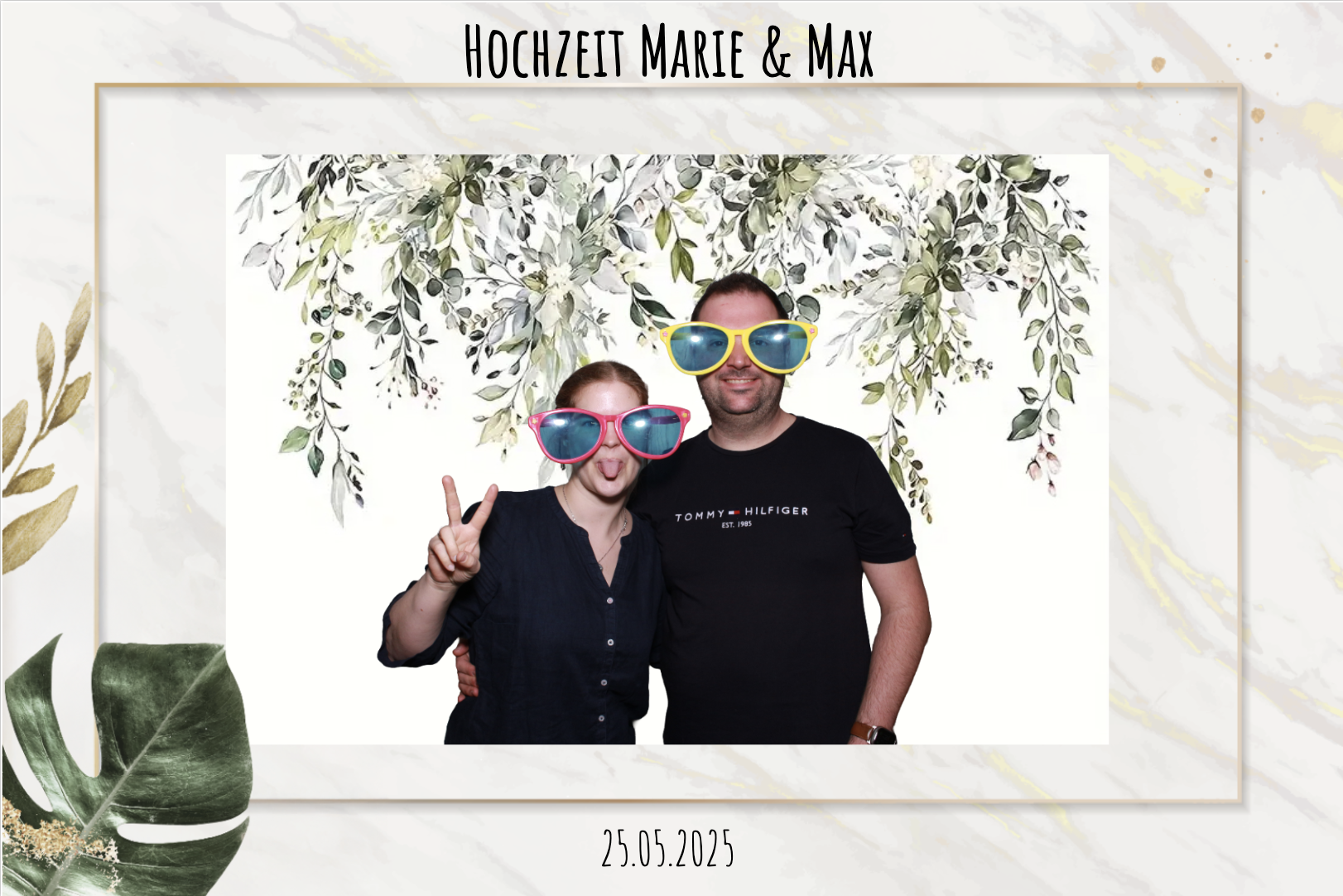 Ein Paar bei einer Hochzeitsfeier trägt große, bunte Sonnenbrillen. Der Hintergrund ist eine weiße Tapete mit botanischem Dekor. Über dem Bild steht 'Hochzeit Marie & Max', und darunter das Datum 25.05.2025.