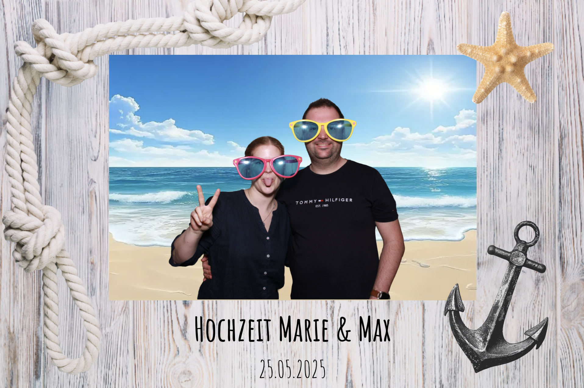 Ein Paar in bunten Sonnenbrillen posiert an einem Strand mit Meer, Himmel und Wolken im Hintergrund. Der Rahmen hat maritime Dekorationen wie Seil, Anker und eine Muschel. Text auf dem Bild: "Hochzeit Marie & Max" und das Datum "25.05.2025".