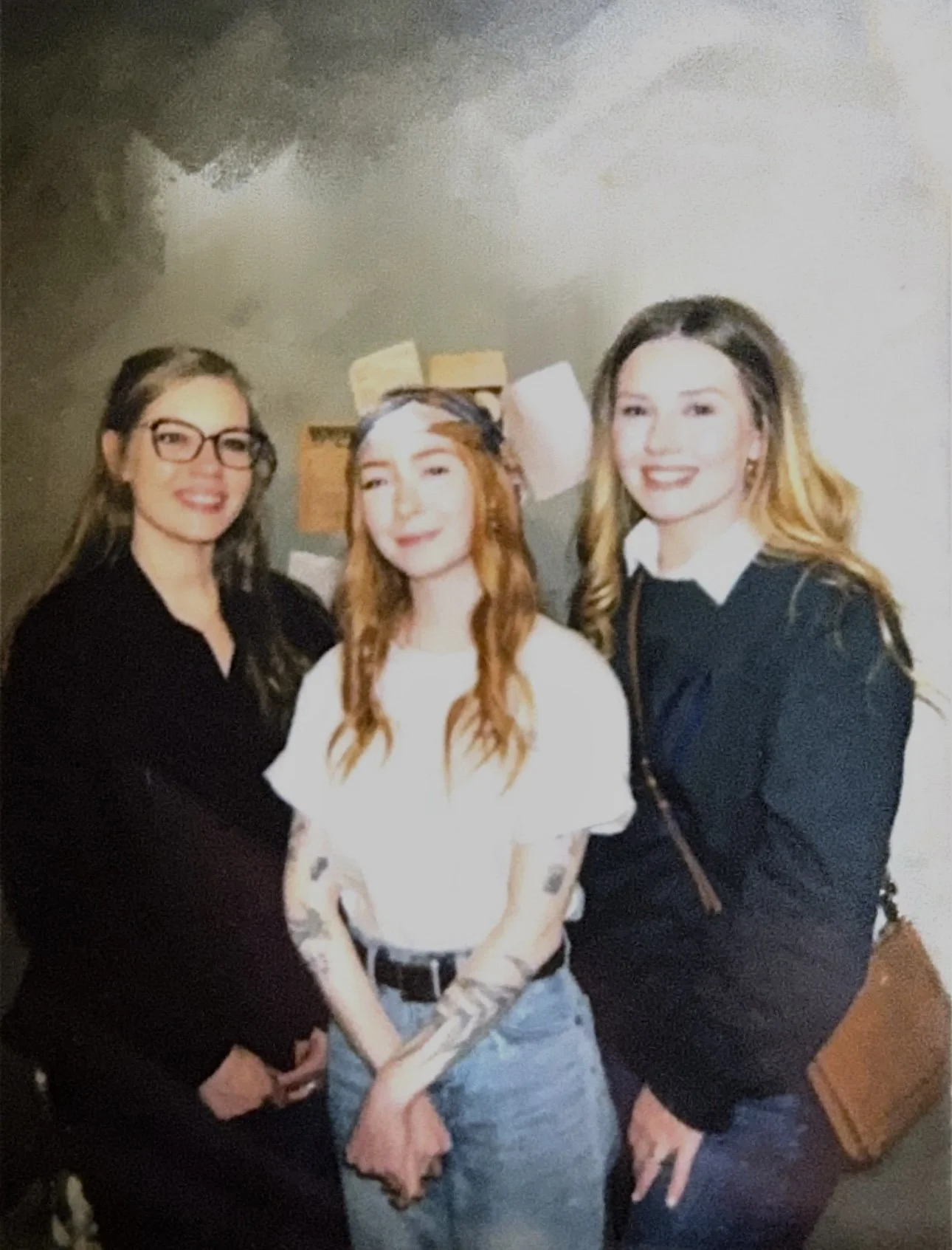 Three young women smiling and posing together indoors.