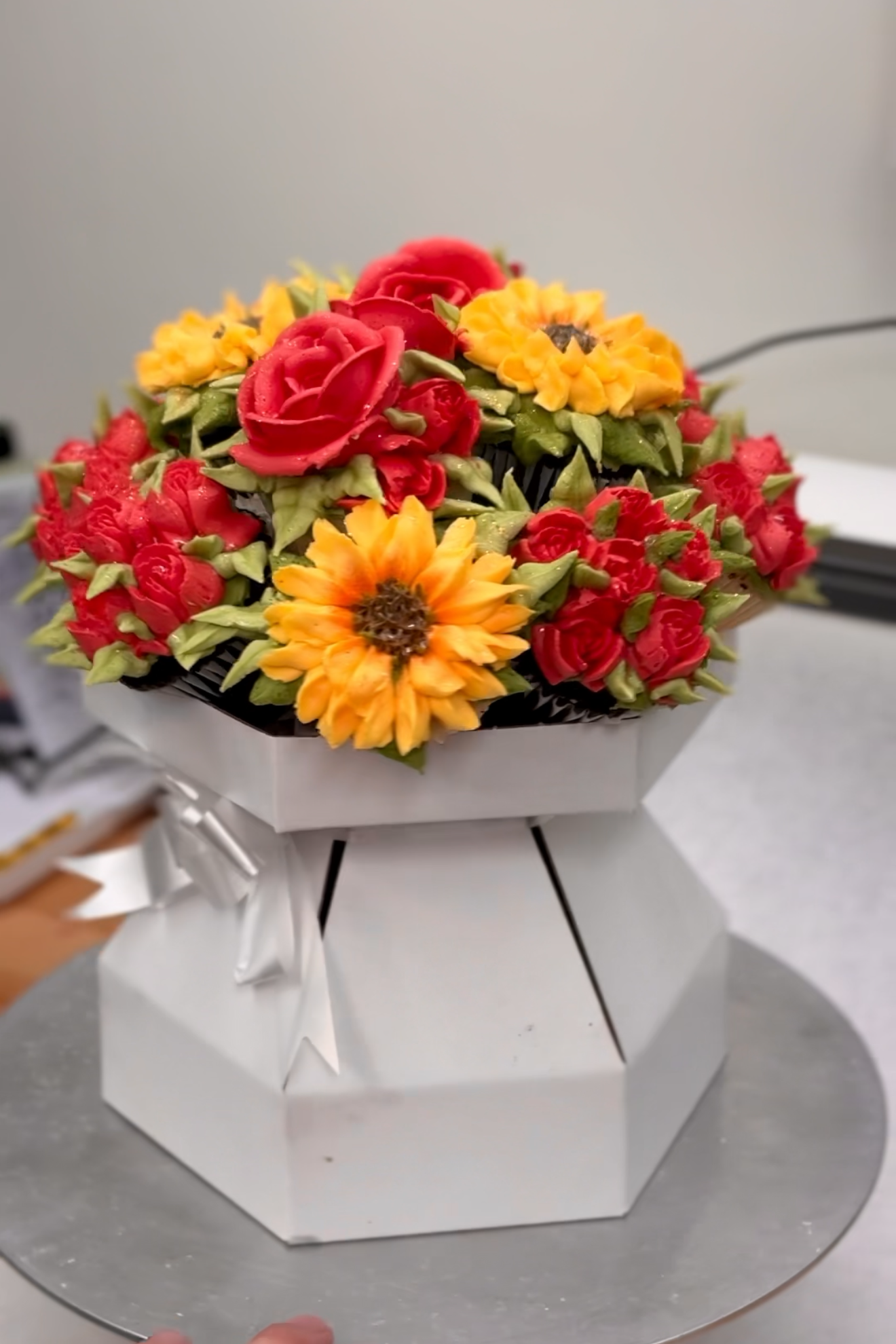 A floral arrangement with red roses, yellow sunflowers, and red berries, wrapped in silver and white paper.
