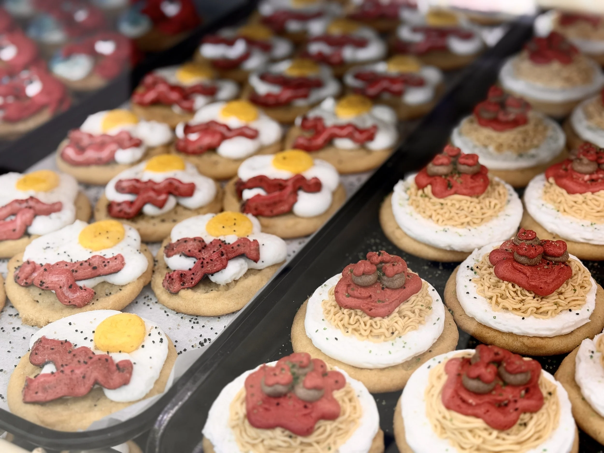 Assorted decorated Christmas cookies with holiday themes, including fried eggs, red and green icing, and various sprinkles, displayed on trays.