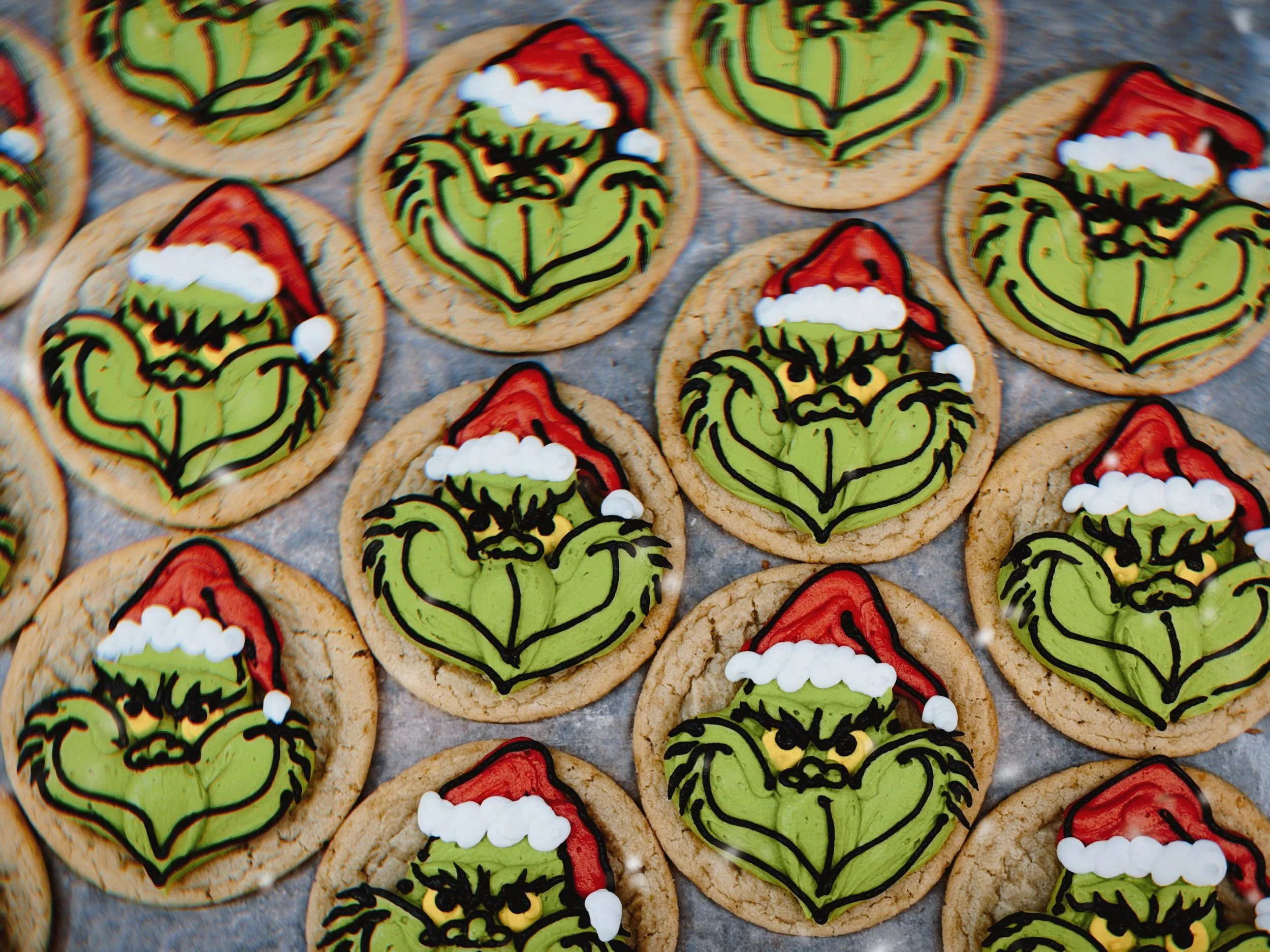 Decorated Christmas-themed sugar cookies with holly leaves, berries, and Santa hats on a baking sheet.