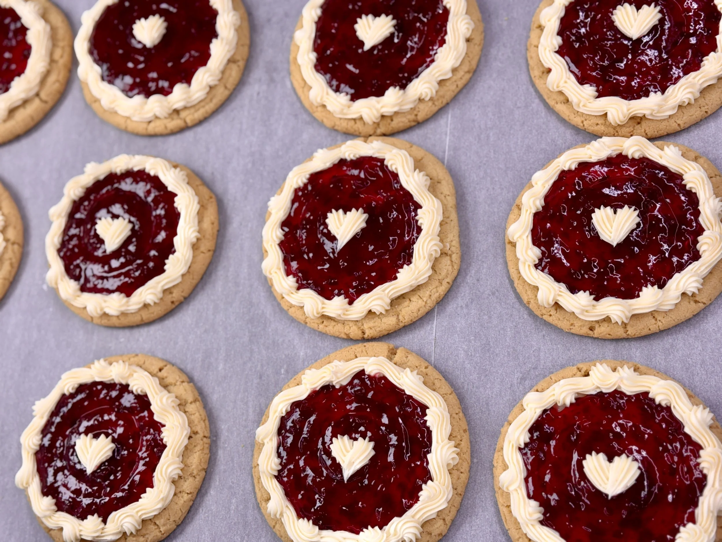 Several cookies with a red jam or jelly center, decorated with white icing around the edges.