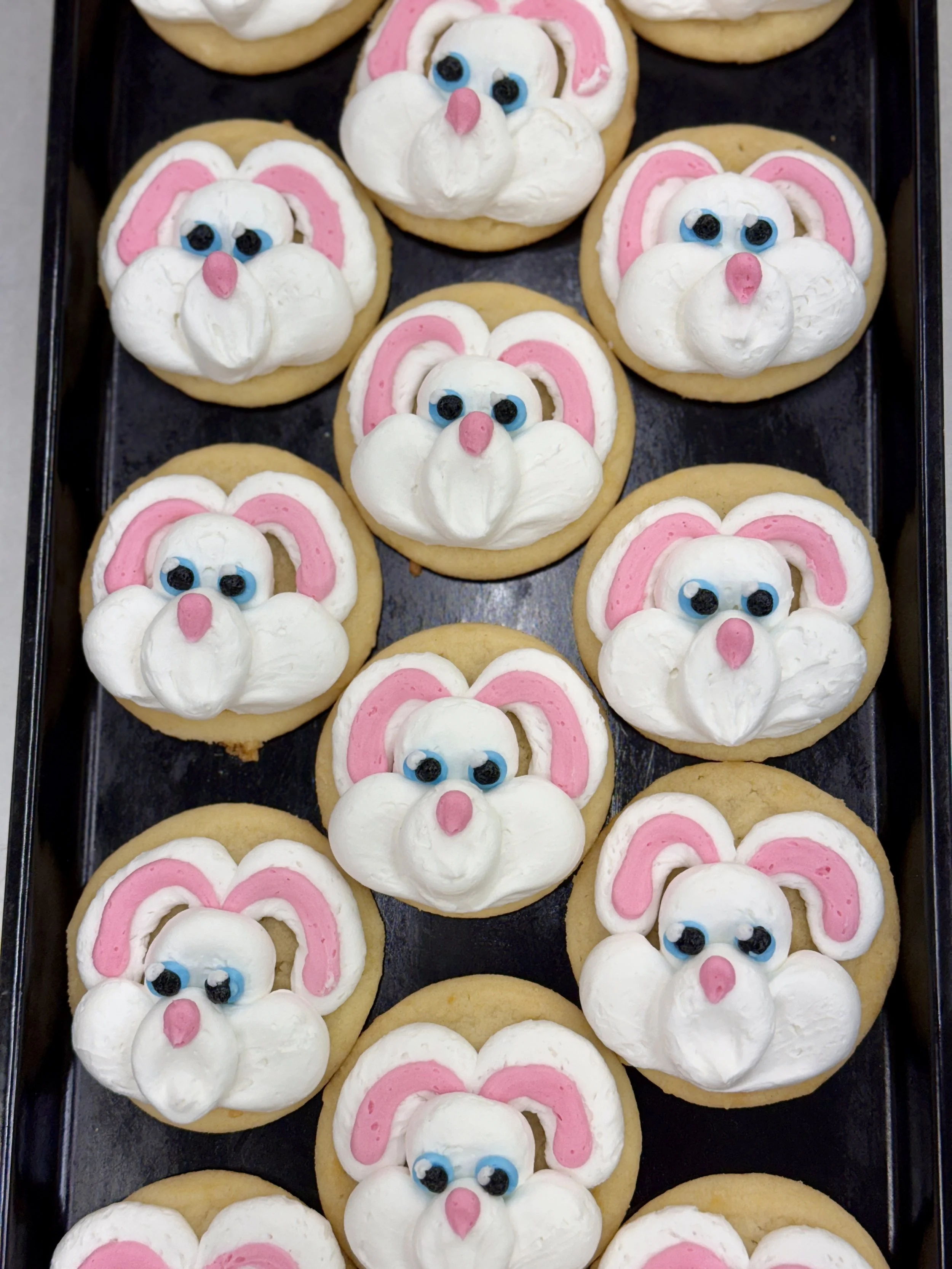 Tray of cookies decorated to look like bunny faces with pink ears, blue eyes, and pink noses using frosting and candy.