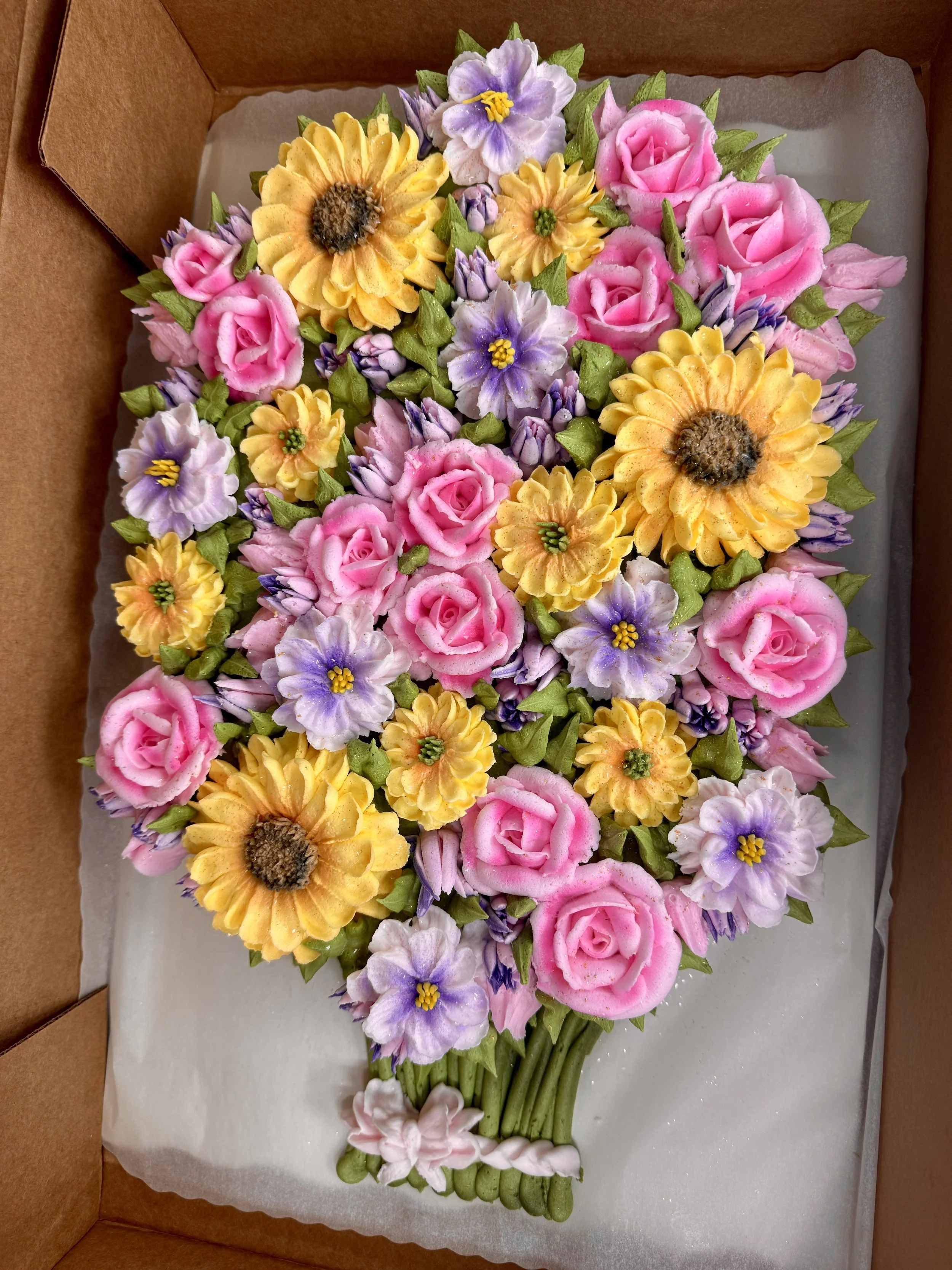 Decorative bouquet of sugar flowers resembling pink roses, yellow sunflowers, and purple violets, arranged in a bouquet.