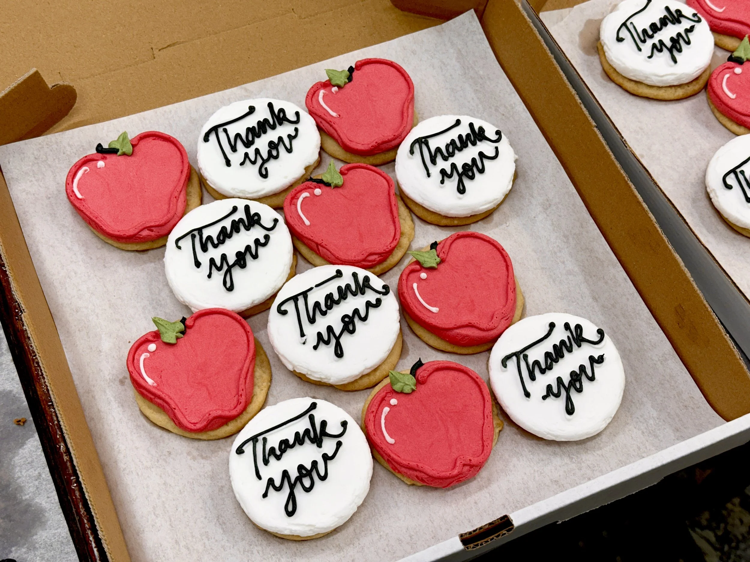 A box of decorated cookies with two designs: red strawberries with green leaves and white circles with the words 'Thank You' written in black icing.