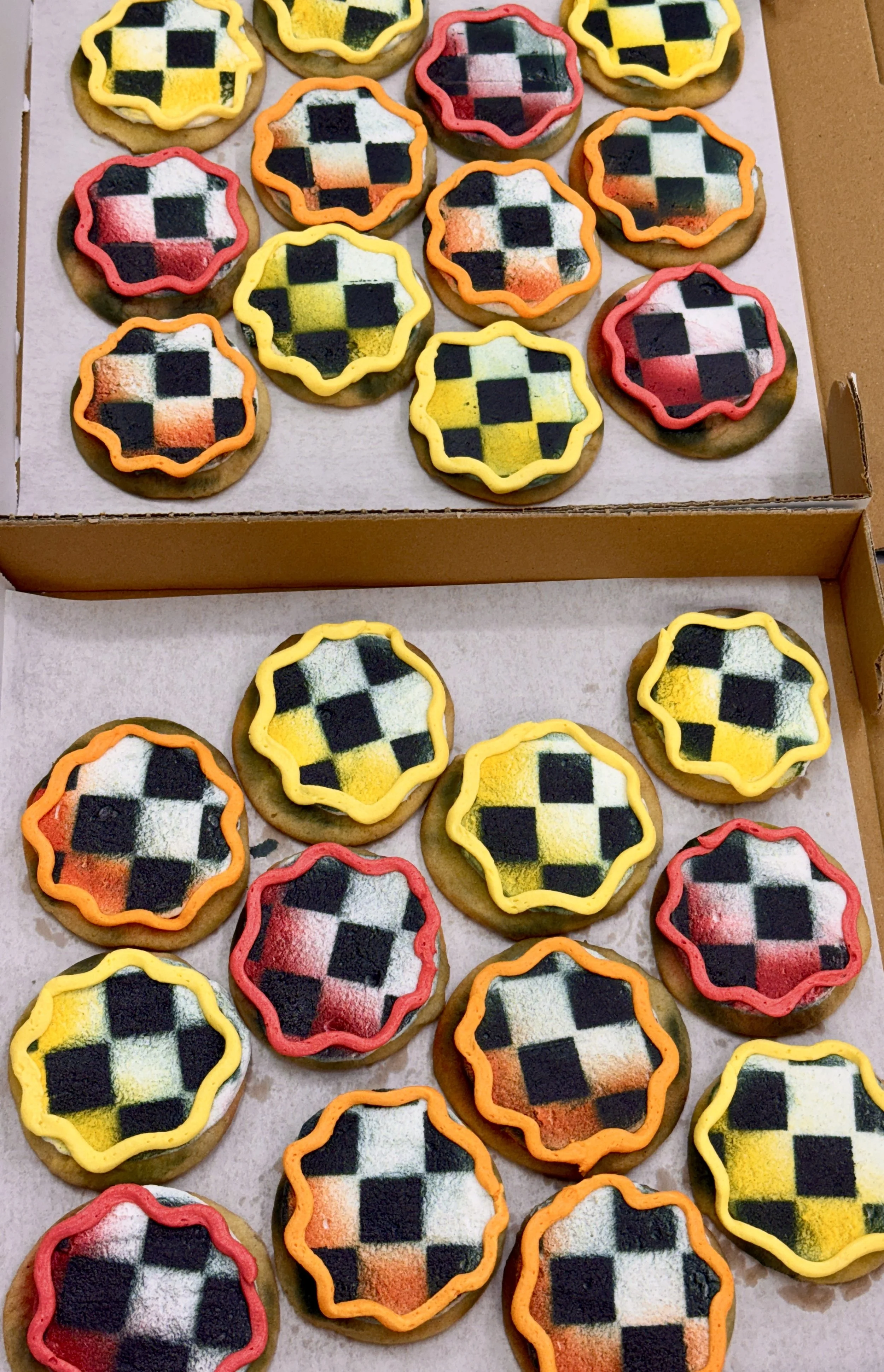 Assorted decorated cookies with pixelated checkered patterns in yellow, orange, red, and white, decorated with colorful icing borders, displayed on a tray.