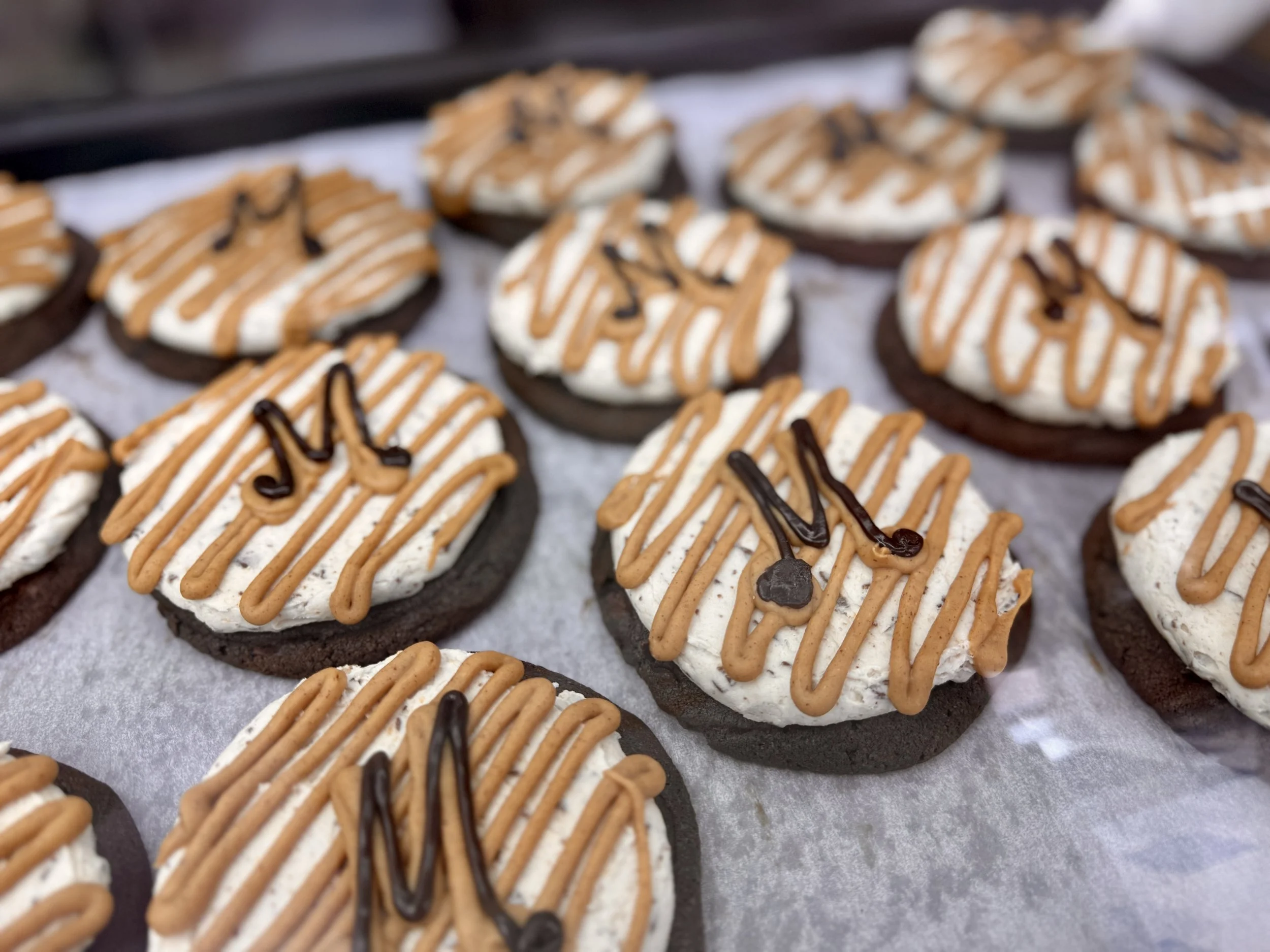 Close-up of ice cream sandwiches with chocolate cookies, vanilla ice cream, and drizzled caramel and chocolate on top.