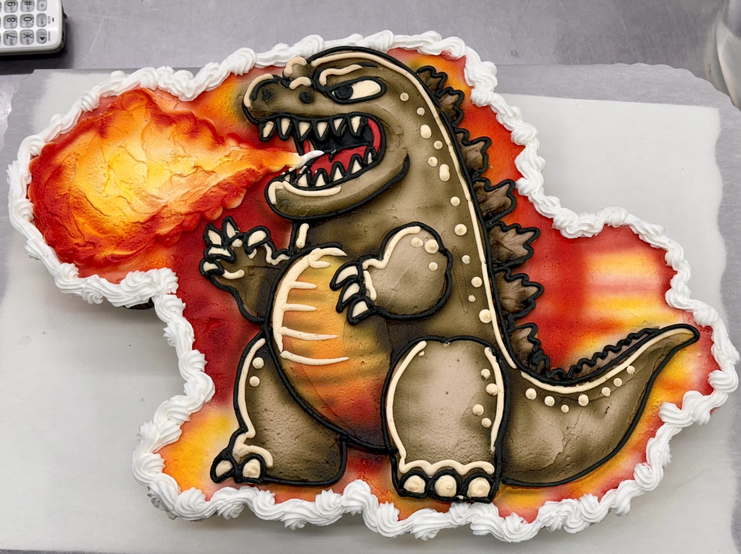 A rectangular birthday cake decorated with a colorful fire and a dinosaur figure made out of icing.