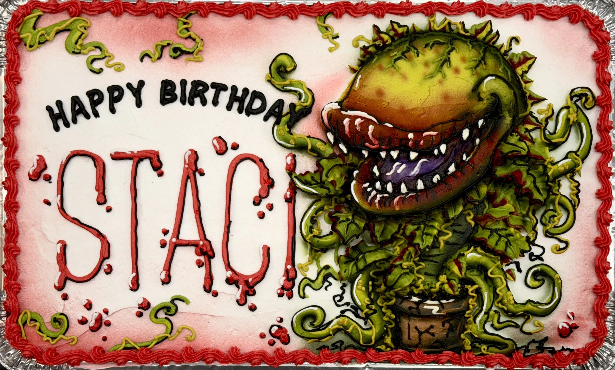 A rectangular birthday cake decorated with cartoon-style artwork of a green dinosaur with purple accents, sharp teeth, and spikes, along with green and yellow squiggly icing. The cake has a red piping border and the words 'HAPPY BIRTHDAY' written in 