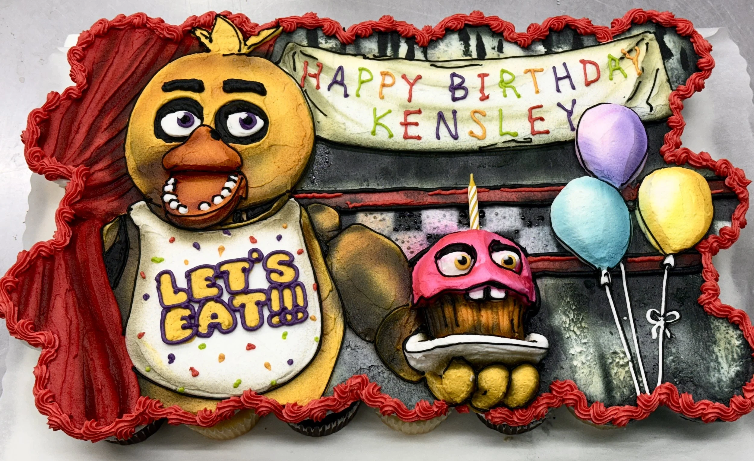 A decorated birthday cake with cartoon character themes, featuring a large yellow bird with purple eyes, balloons, and colorful candles. The cake has a red border and a message that reads 'HAPPY BIRTHDAY KENSLEY' on a banner.