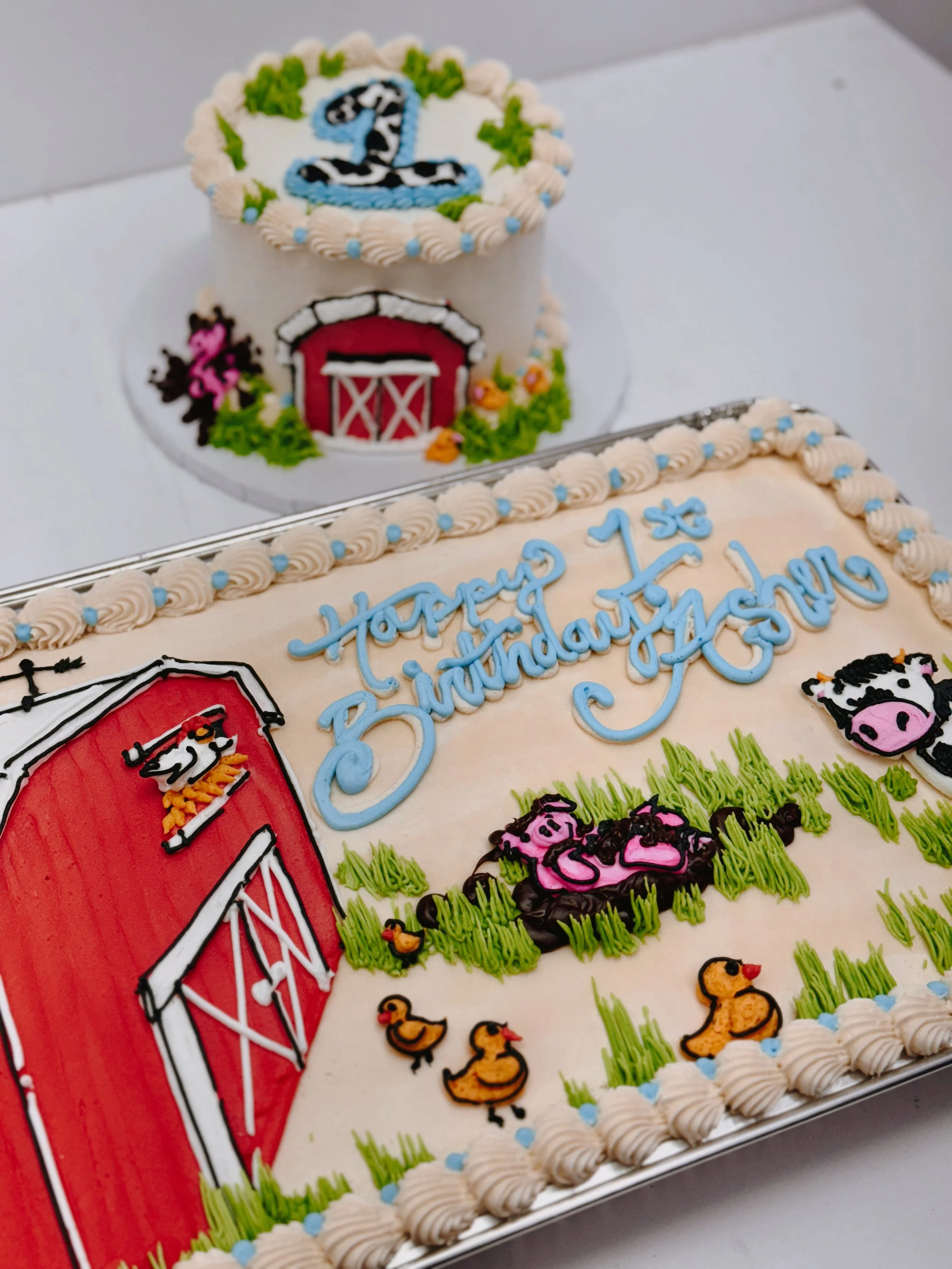 Decorated birthday cake with farm theme, featuring a red barn, yellow ducklings, a green field, and a blue and white 