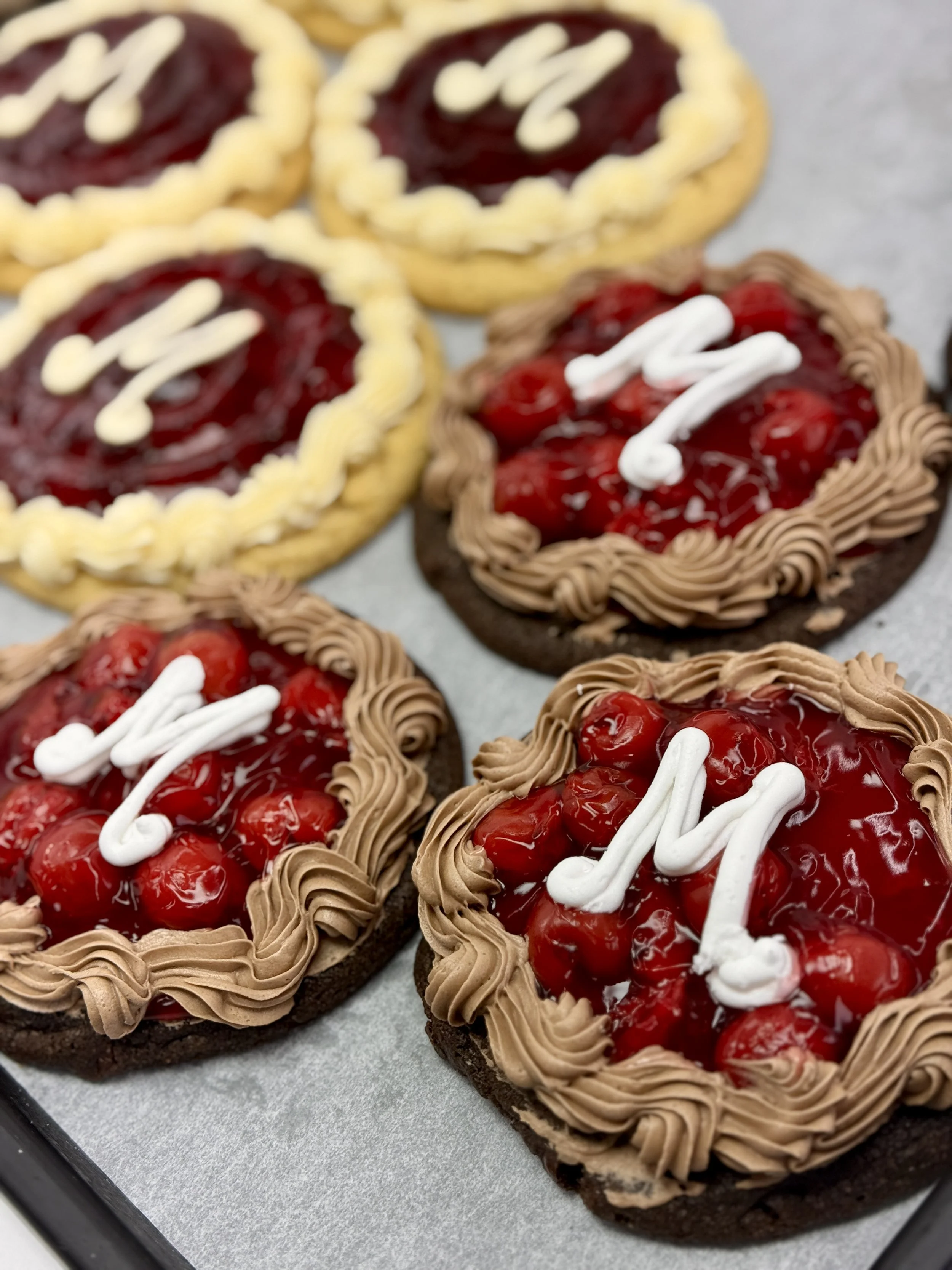 Chocolate cookies with red fruit topping, upside down, decorated with white and brown icing.