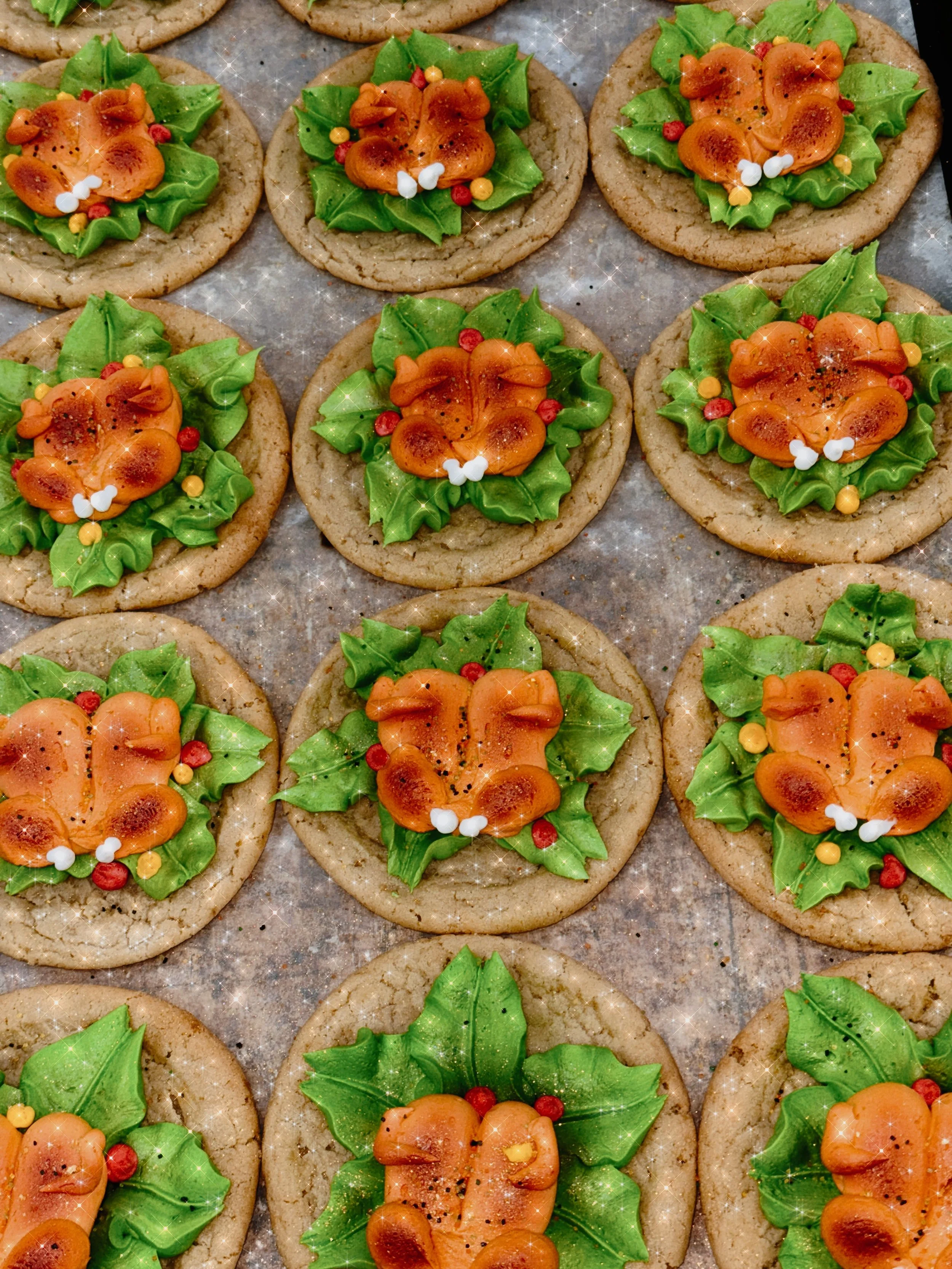 Holiday cookies decorated with green icing leaves, orange frosting shaped like pumpkins, small white, red, and yellow edible beads, and black sprinkles on a baking sheet.