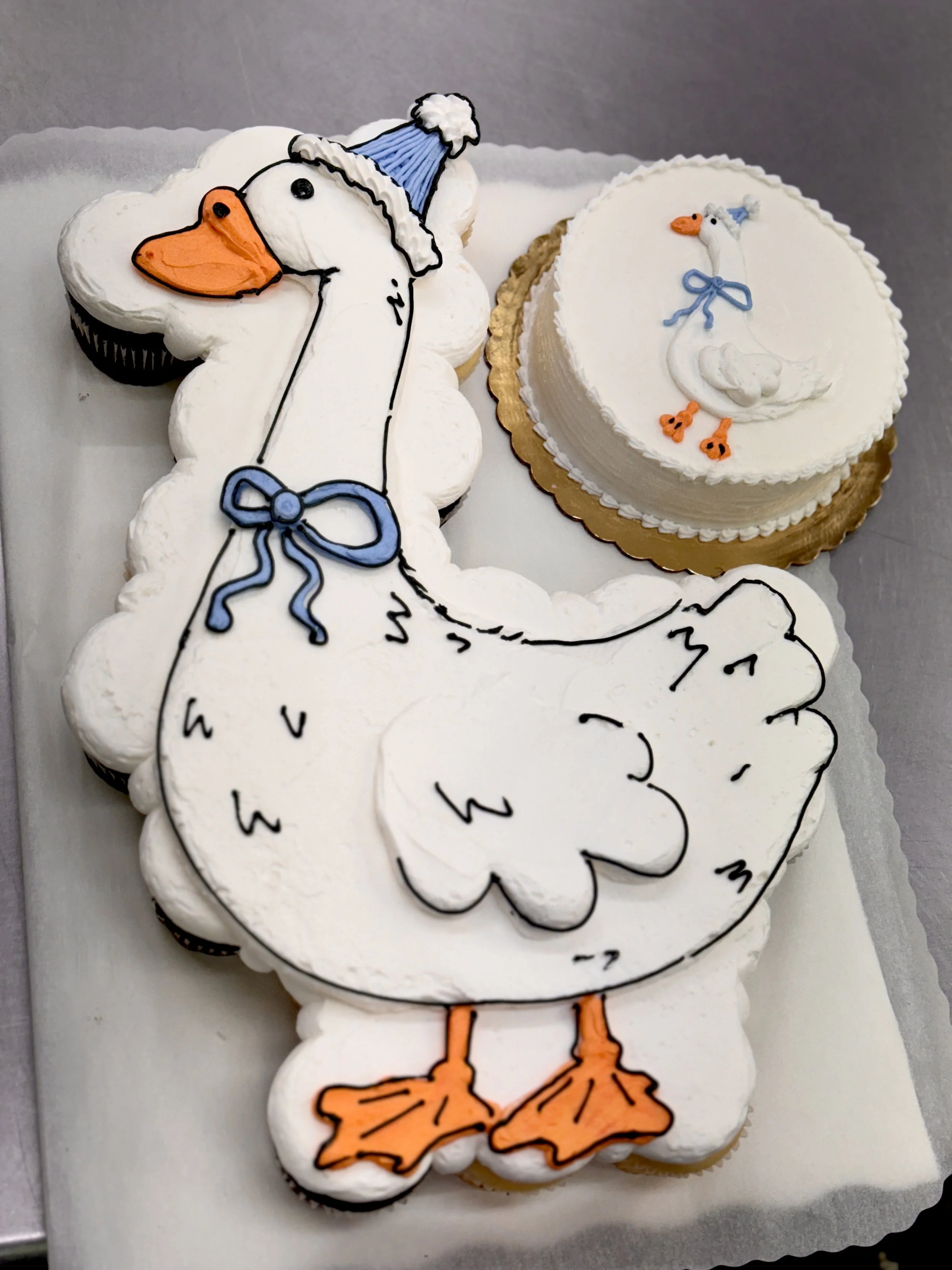 Cookies decorated with a swan wearing a blue hat, with the swallow's legs and beak outlined in orange, and a white body with black outlines.