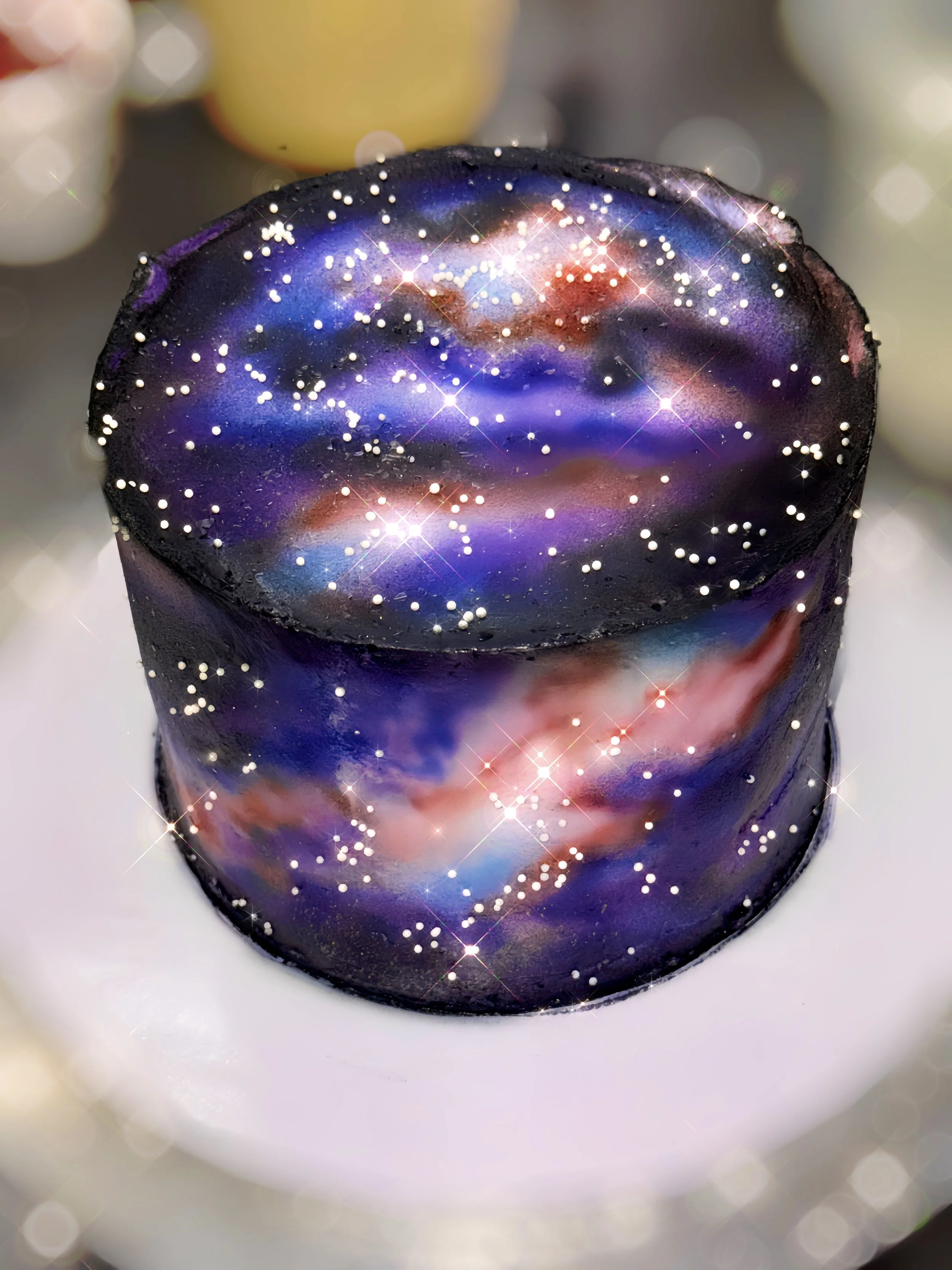 Close-up of a cylindrical object with a galaxy-like pattern featuring stars and nebulae, set against a blurred background.
