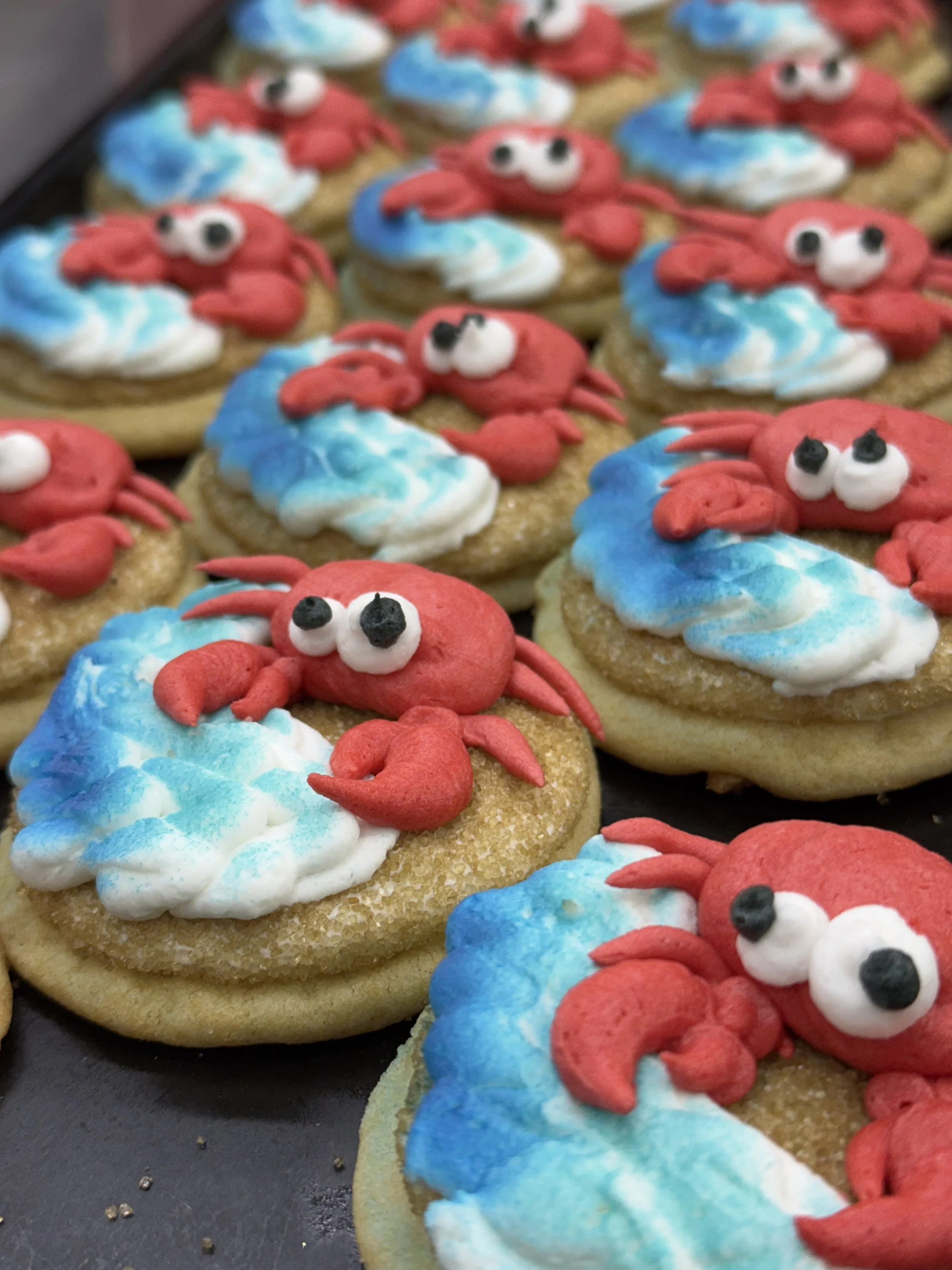 Cookies decorated to look like red crabs with white and black eyes, placed on a dark tray.