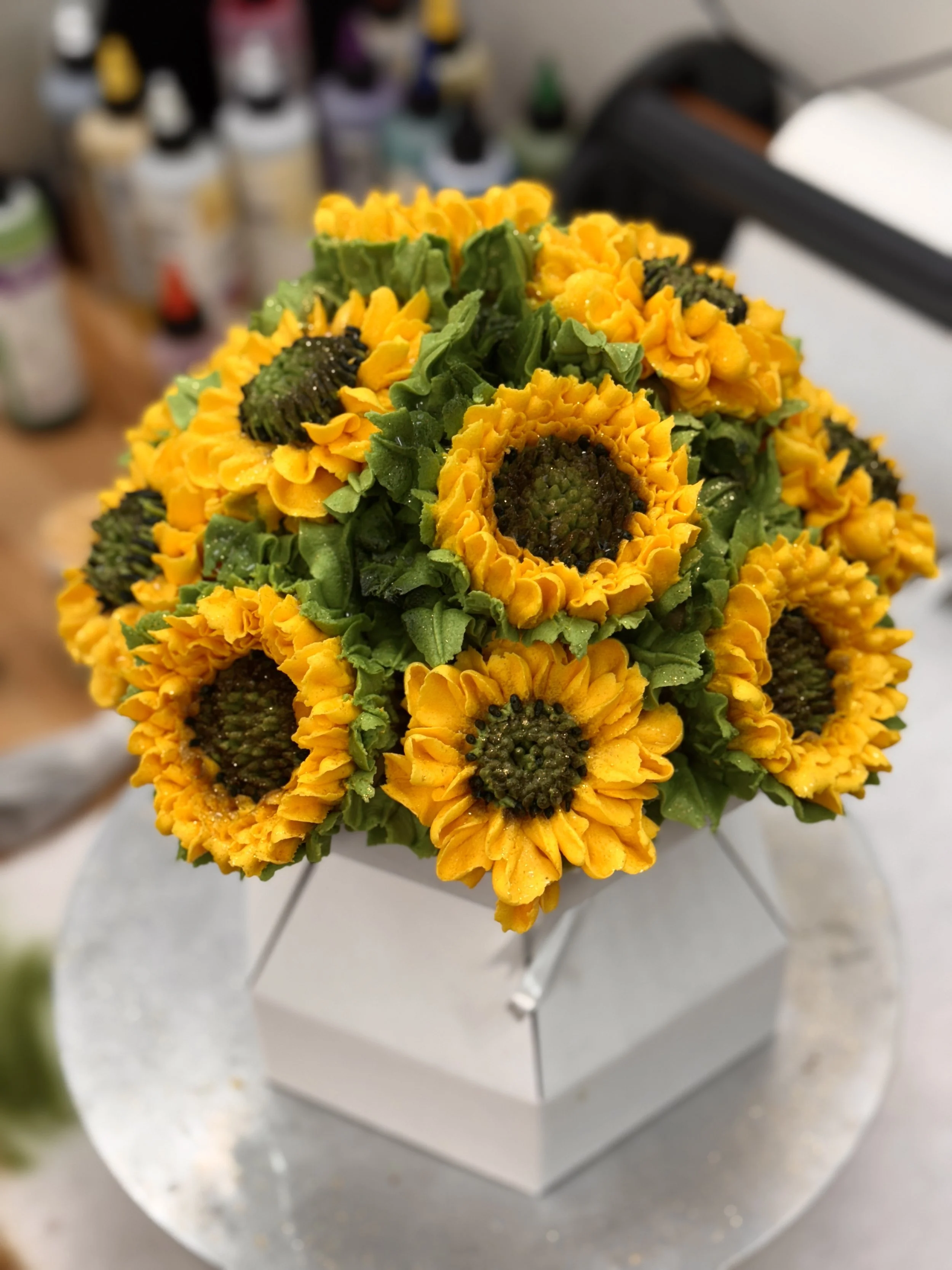 A bouquet of yellow sunflowers with green leaves resting on a silver tray or cake stand.