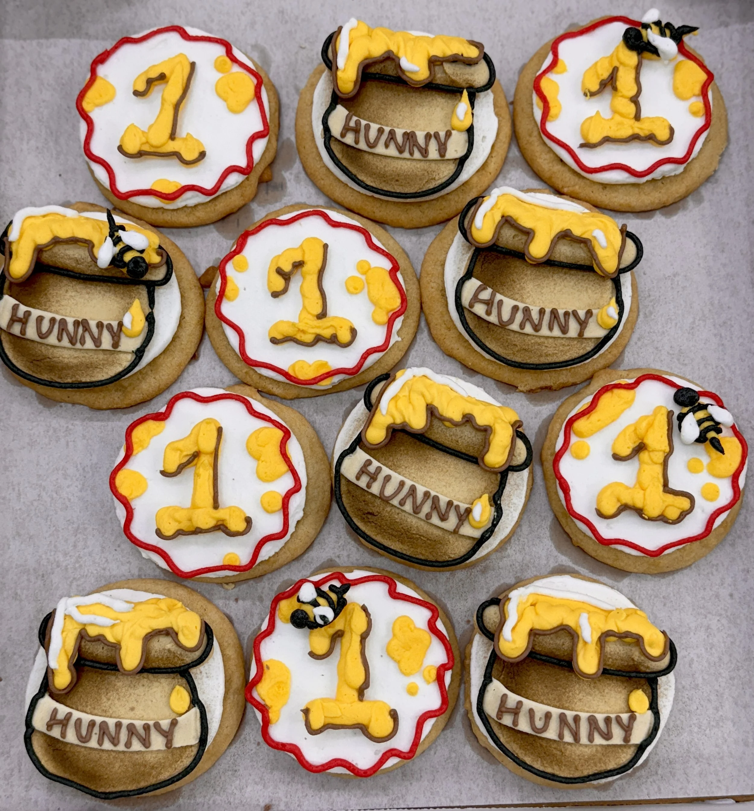 Decorated cookies with number ones, yellow and black bees, and the word 'HUNNY' written on some, for a first birthday celebration.