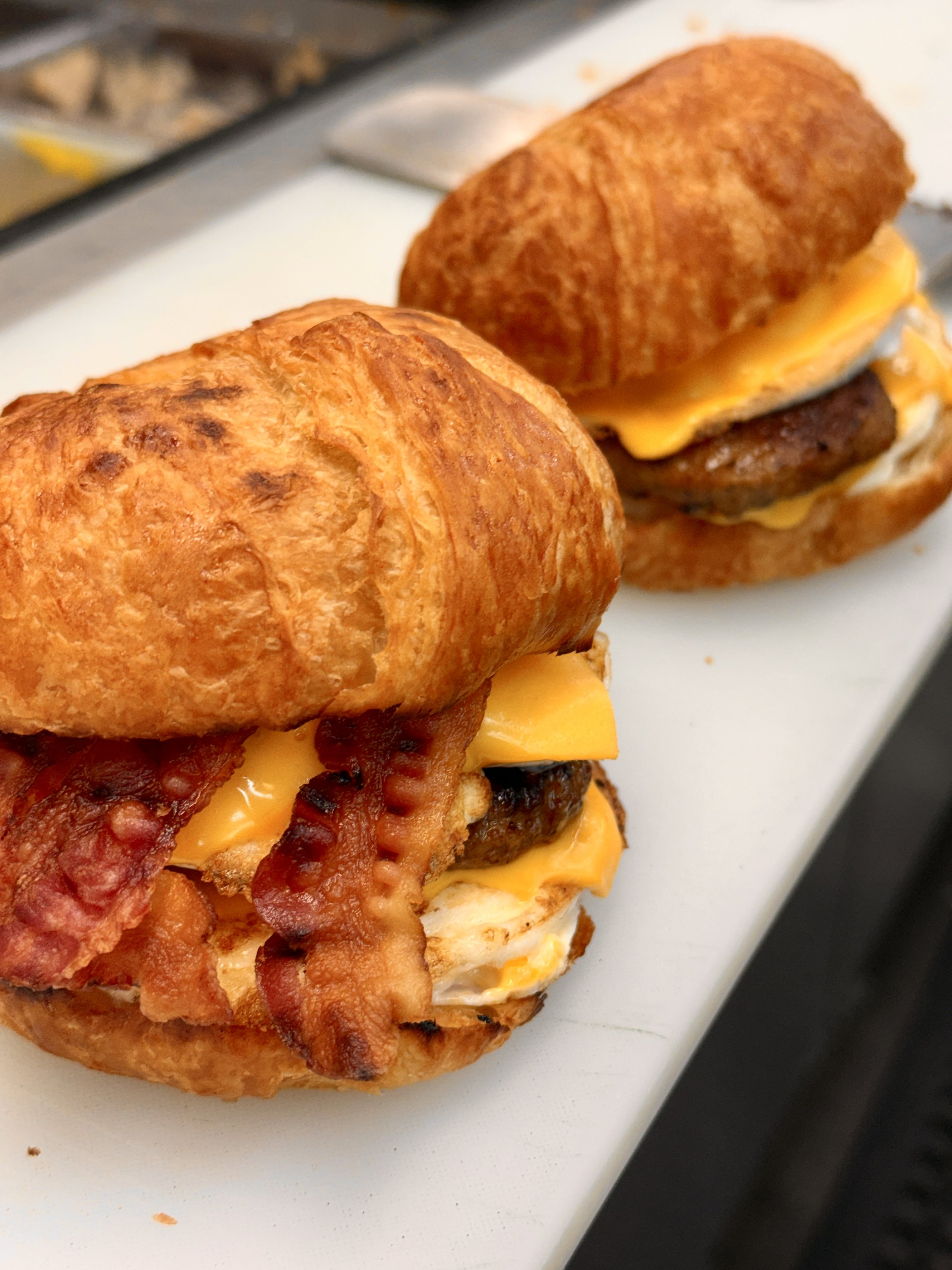 Close-up of a breakfast sandwich with bacon, egg, cheese, and a sausage patty on a toasted bun.