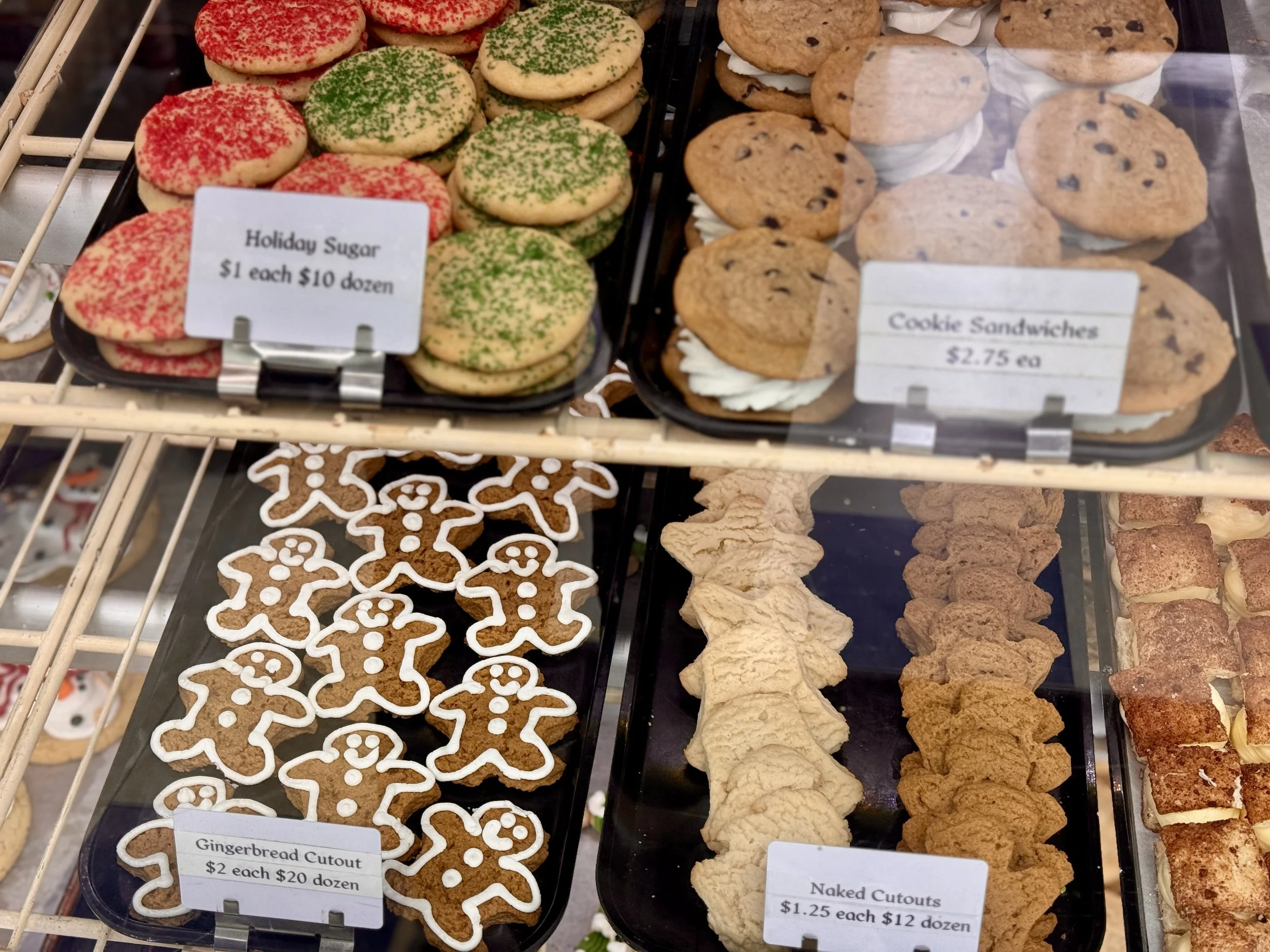 Assorted cookies on display in a bakery case, including gingerbread cutouts, cookie sandwiches, and cookies decorated with red and green sprinkles.