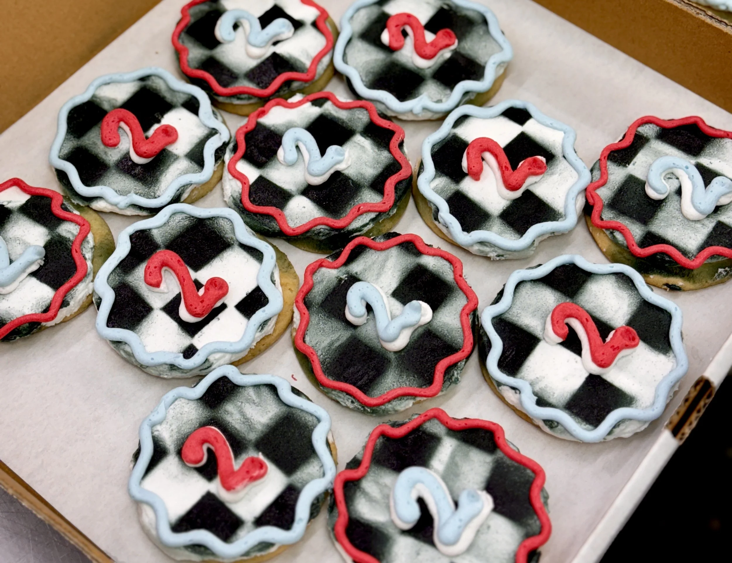 Decorated cookies with black and white checkered pattern, red and blue icing borders, and red and blue icing swirls, arranged on a white surface.