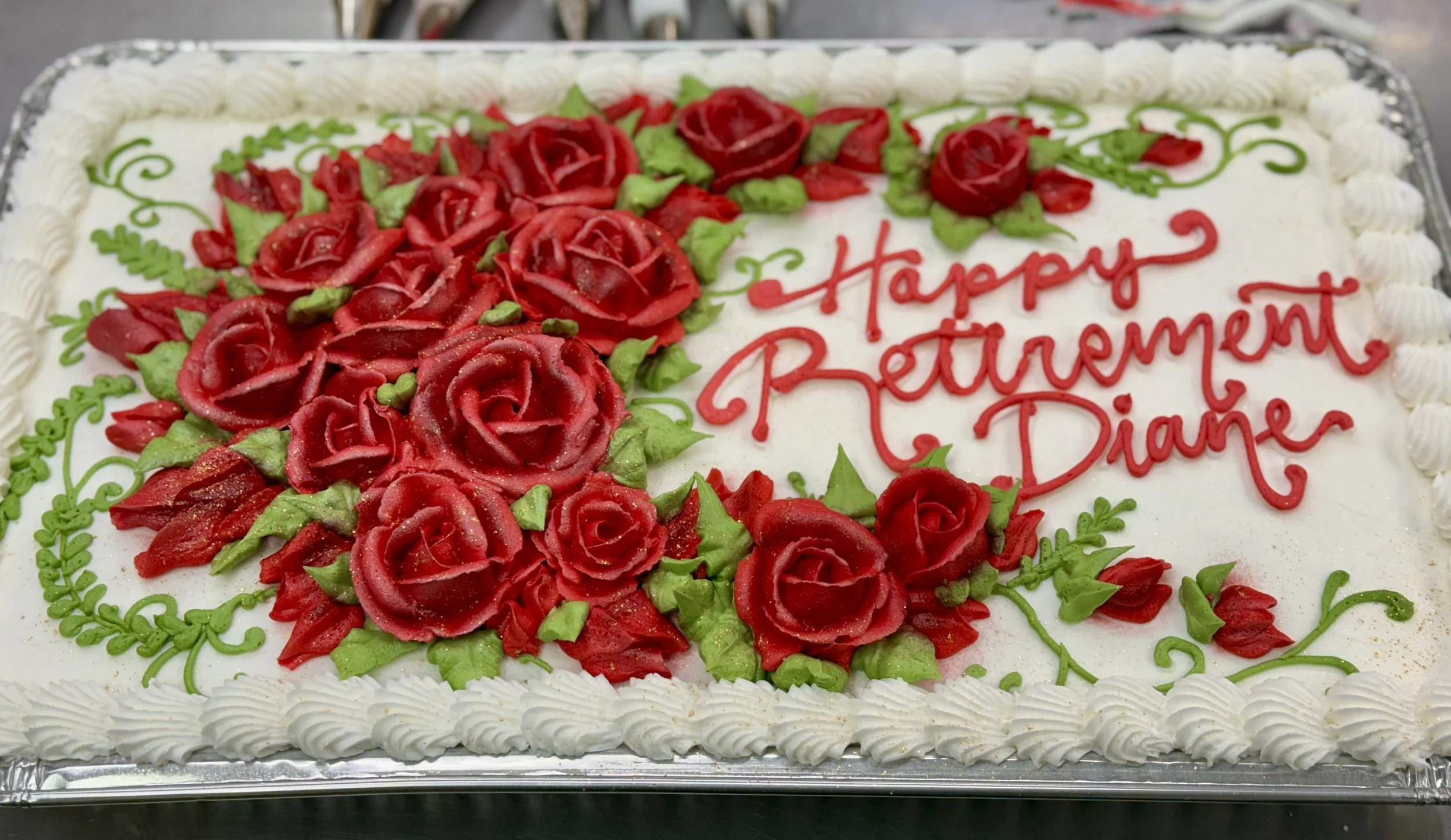 A rectangular wedding cake decorated with red roses and green leaves, with the message "Happy Retirement Diane" written in red icing.