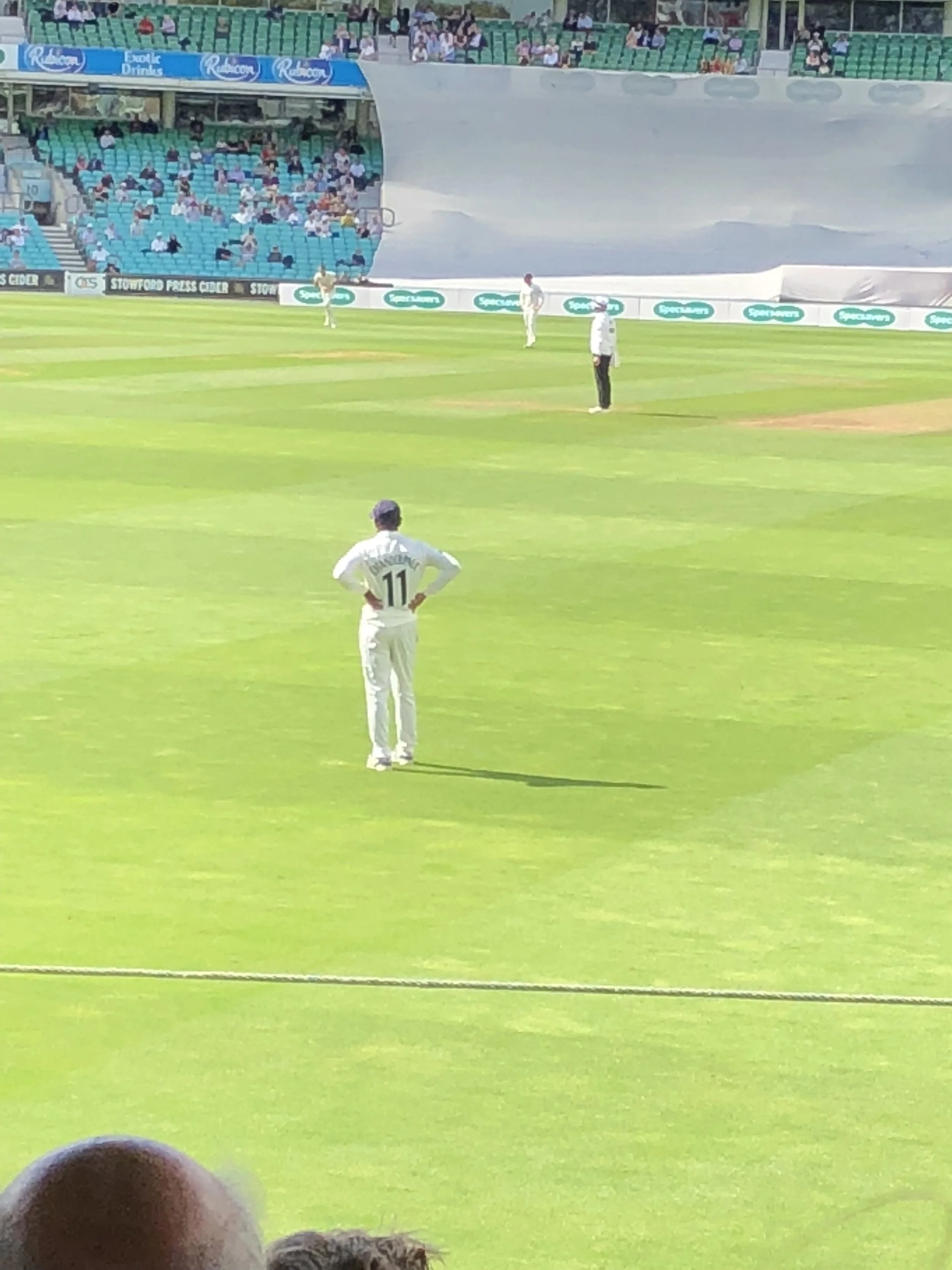 A cricket game taking place in a stadium with players on the field and spectators sitting in the stands.