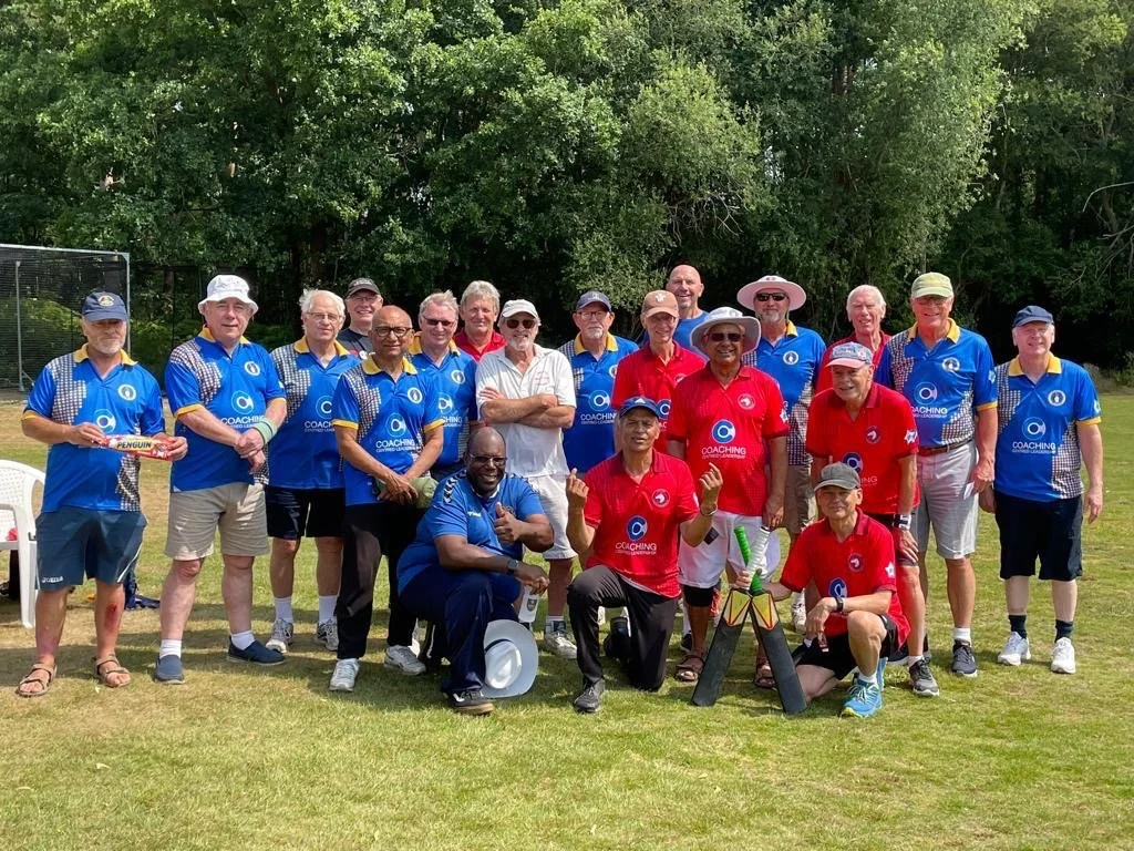 A group of people posing outdoors on a grassy field with trees in the background, some wearing blue shirts and others red shirts, possibly participating in a sports or team event.