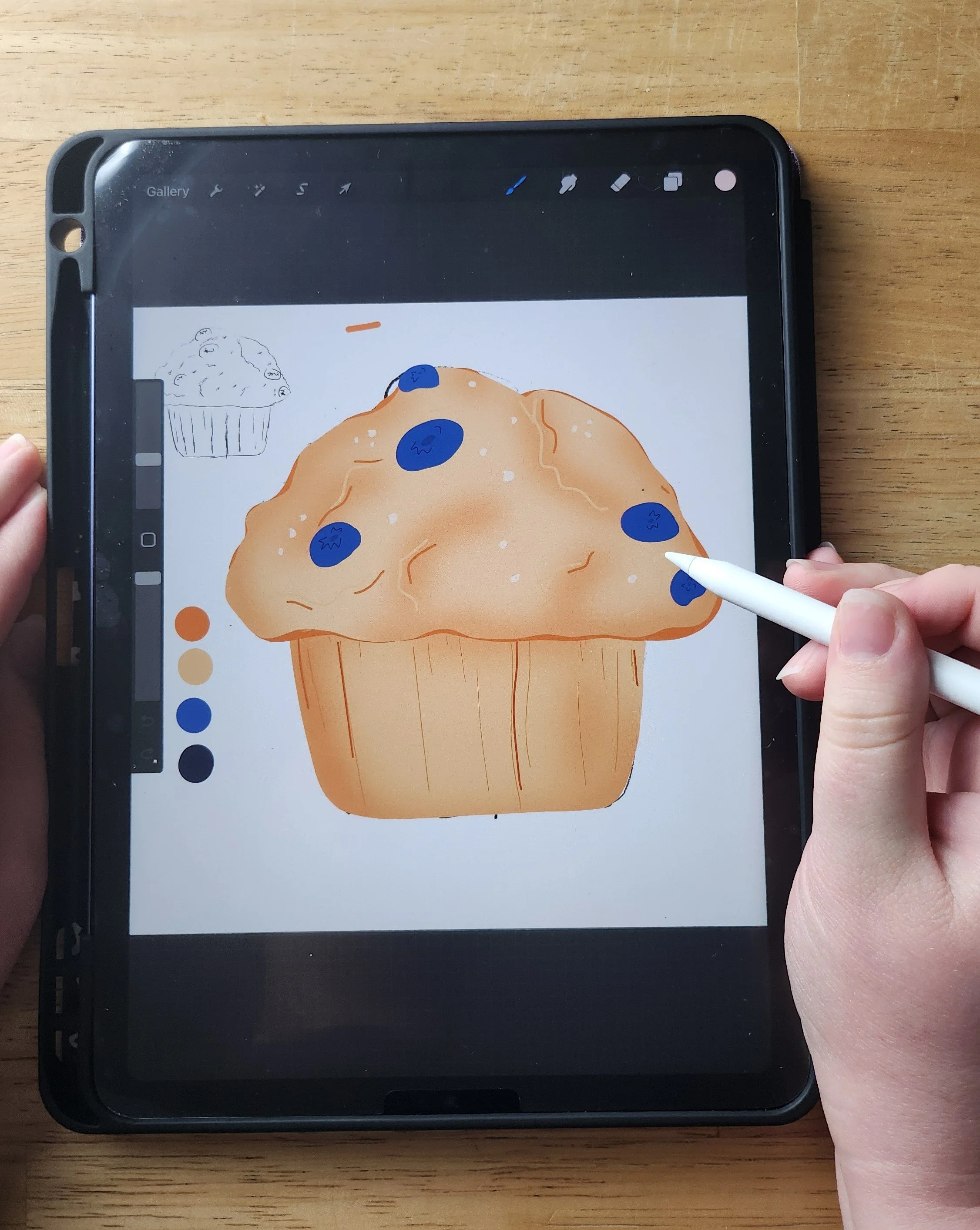Drawing of a blueberry muffin on a tablet screen with a stylus, featuring a digital palette to the left and a smaller, partial muffin sketch in the background.