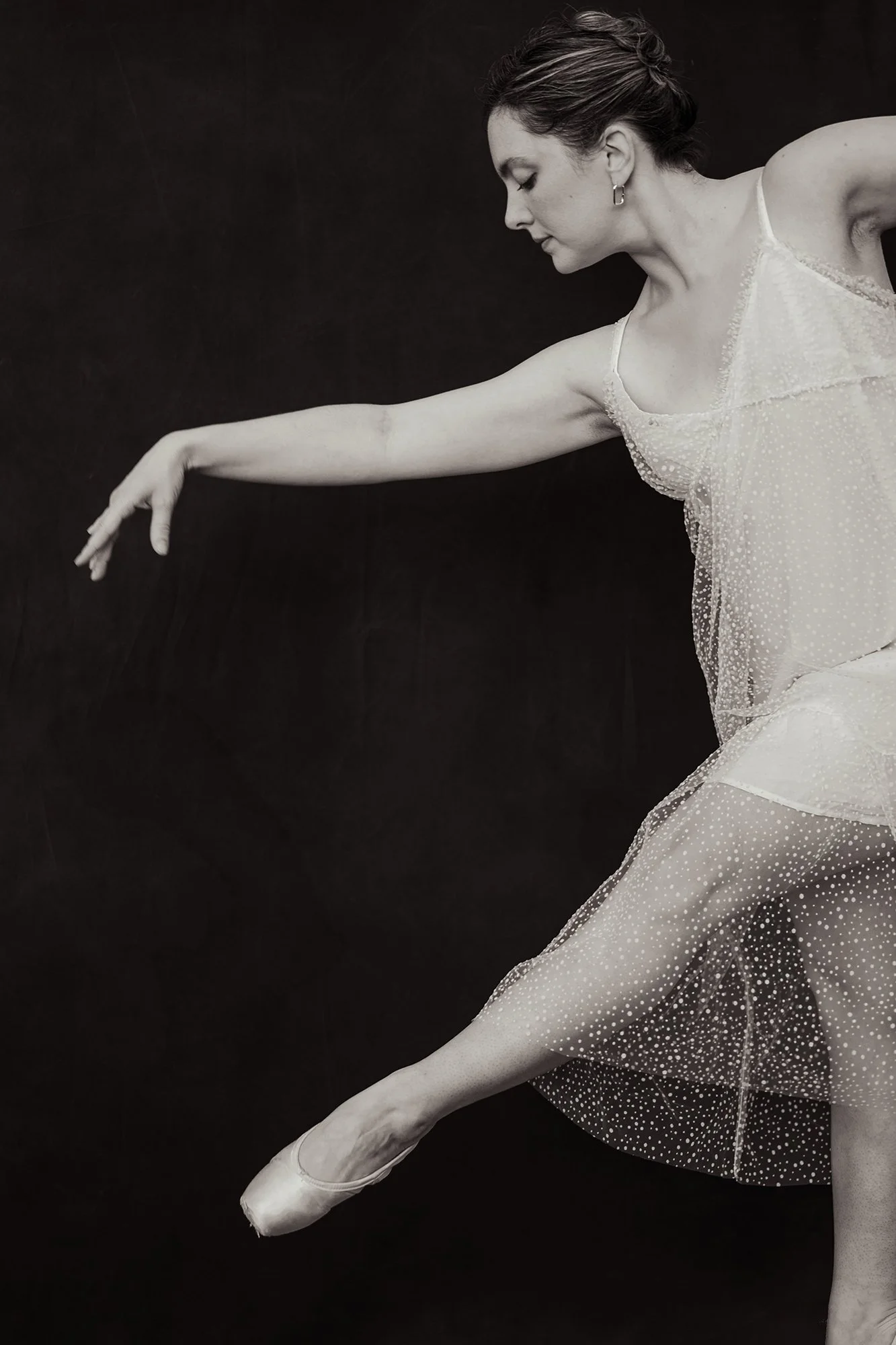A ballerina in a tutu practicing a dance pose on a dark background.