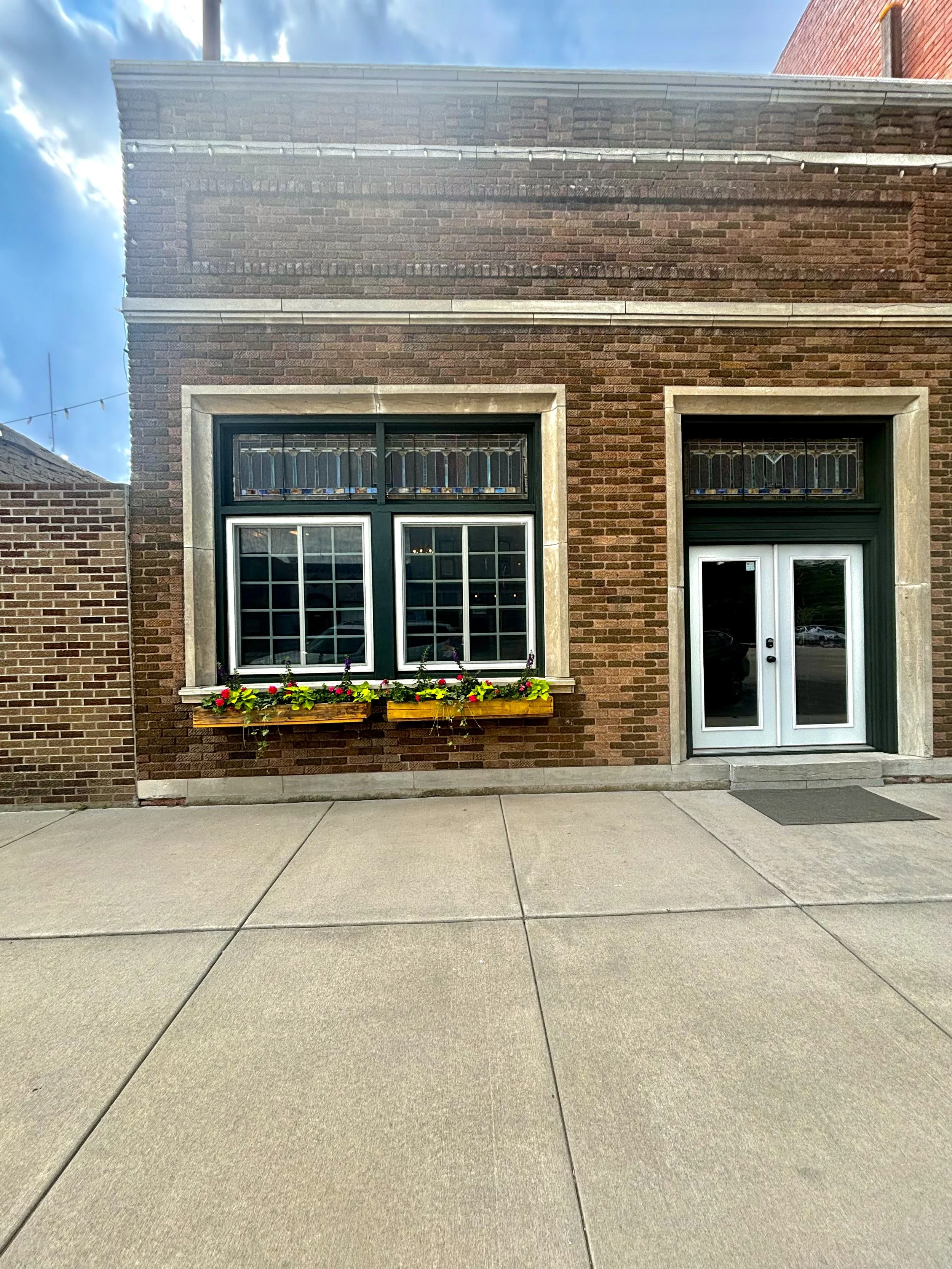 Brick building with a window with a flower box and a glass door, concrete sidewalk in front