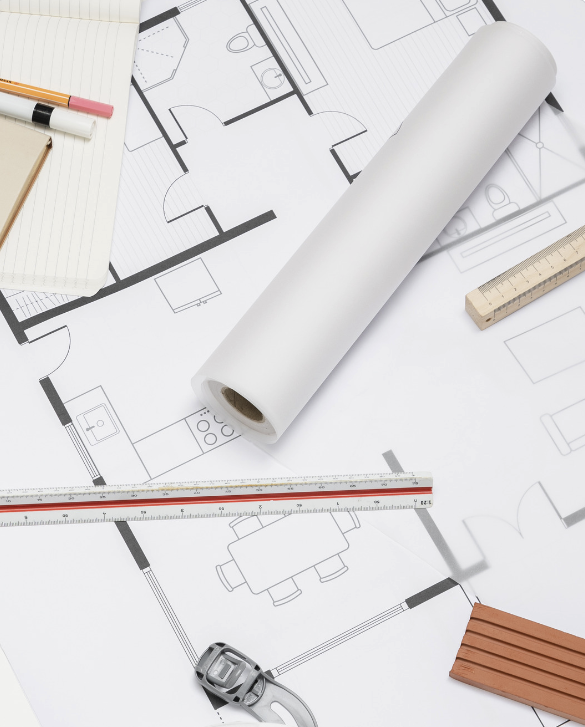 Architectural blueprints, a rolled-up plan, a ruler, a square, a level, a watch, a notepad with pens, and a measuring scale on a white surface.