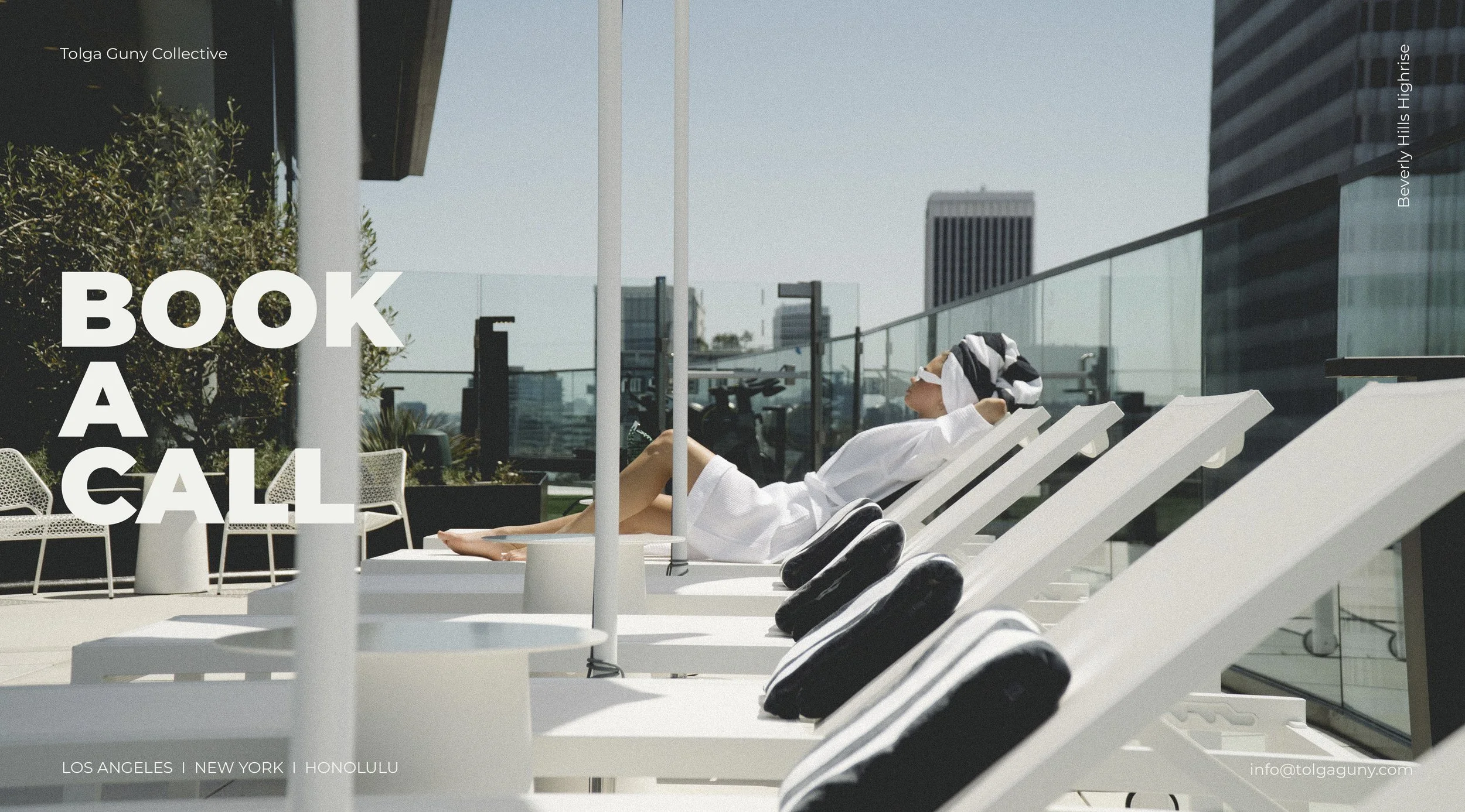 A woman in a white bathrobe and striped headscarf relaxing on a sun lounger on a rooftop patio in Los Angeles, with tall buildings in the background.