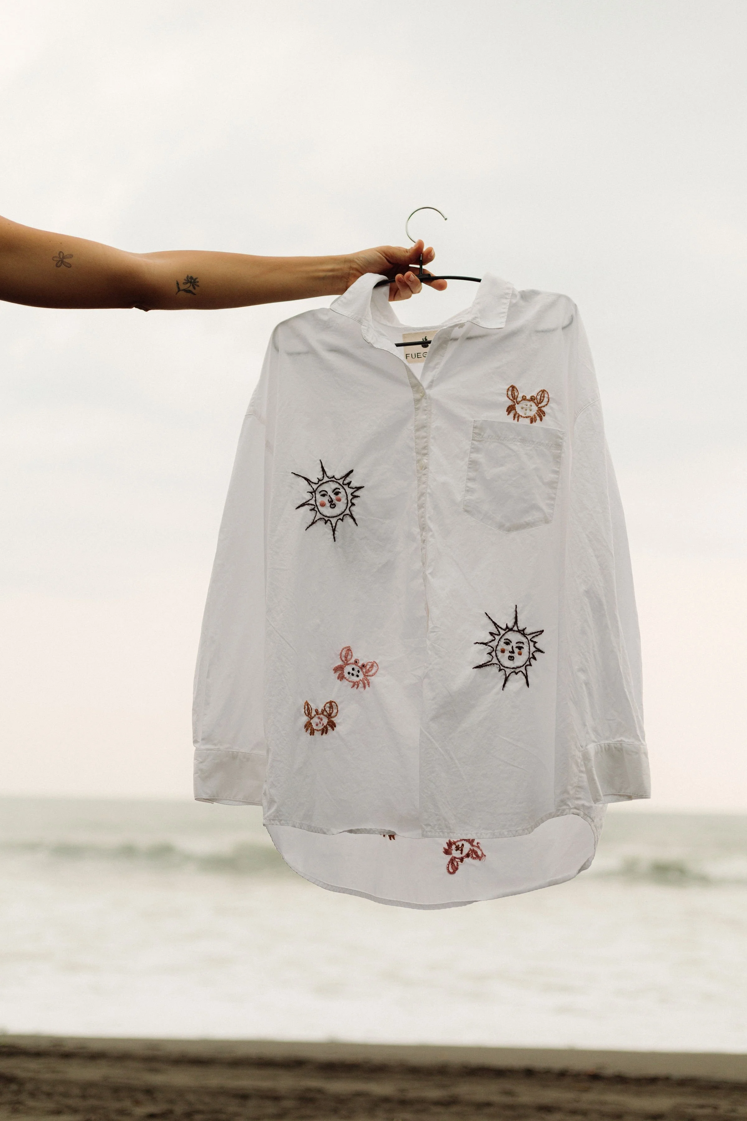 A striped button-up shirt hanging on a hanger with embroidered sun and snowflake designs on a two-tone pastel wall.