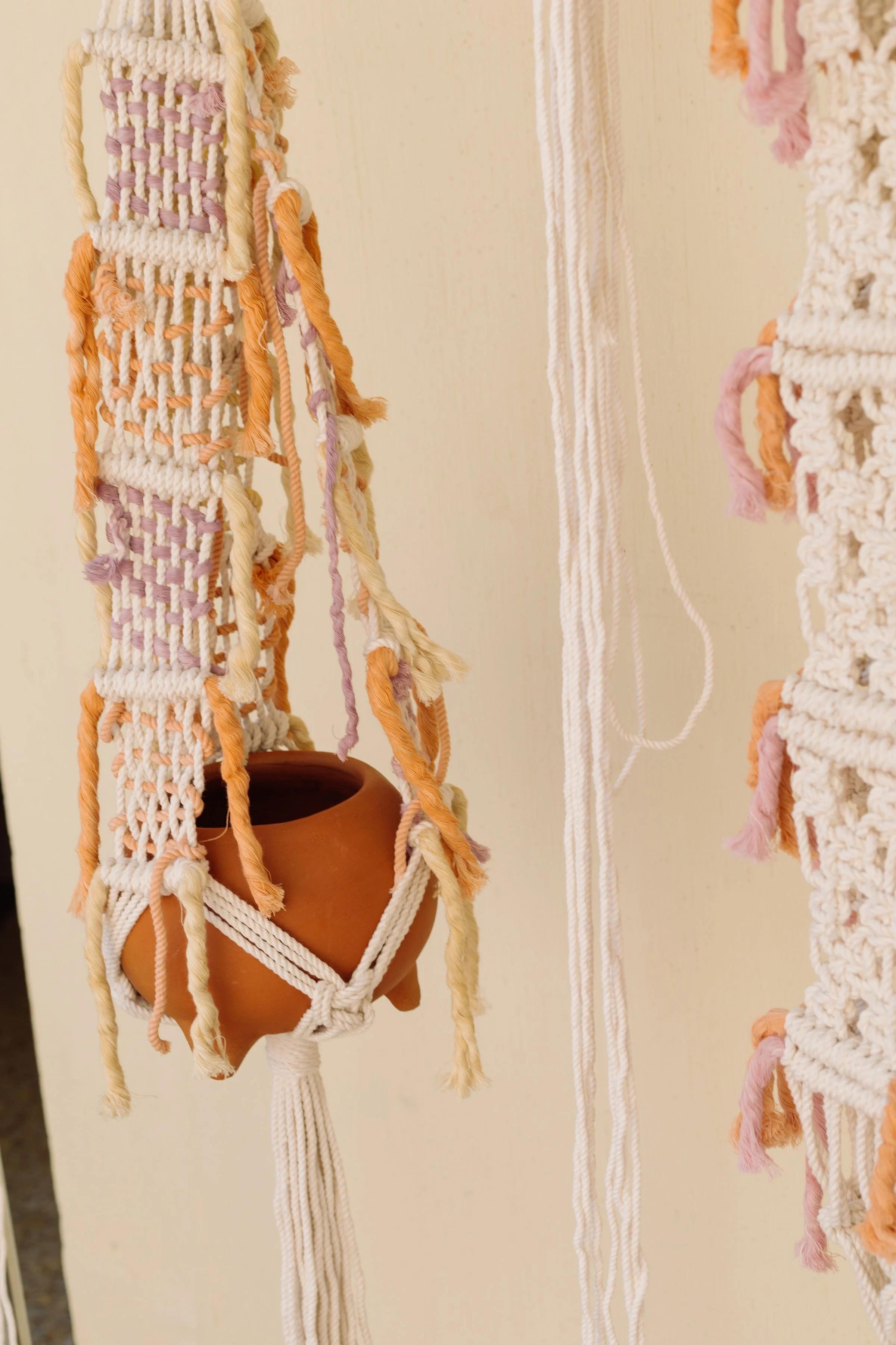 Textured wall hanging with woven patterns and fringes hangs on a blue wall, held by two hands.