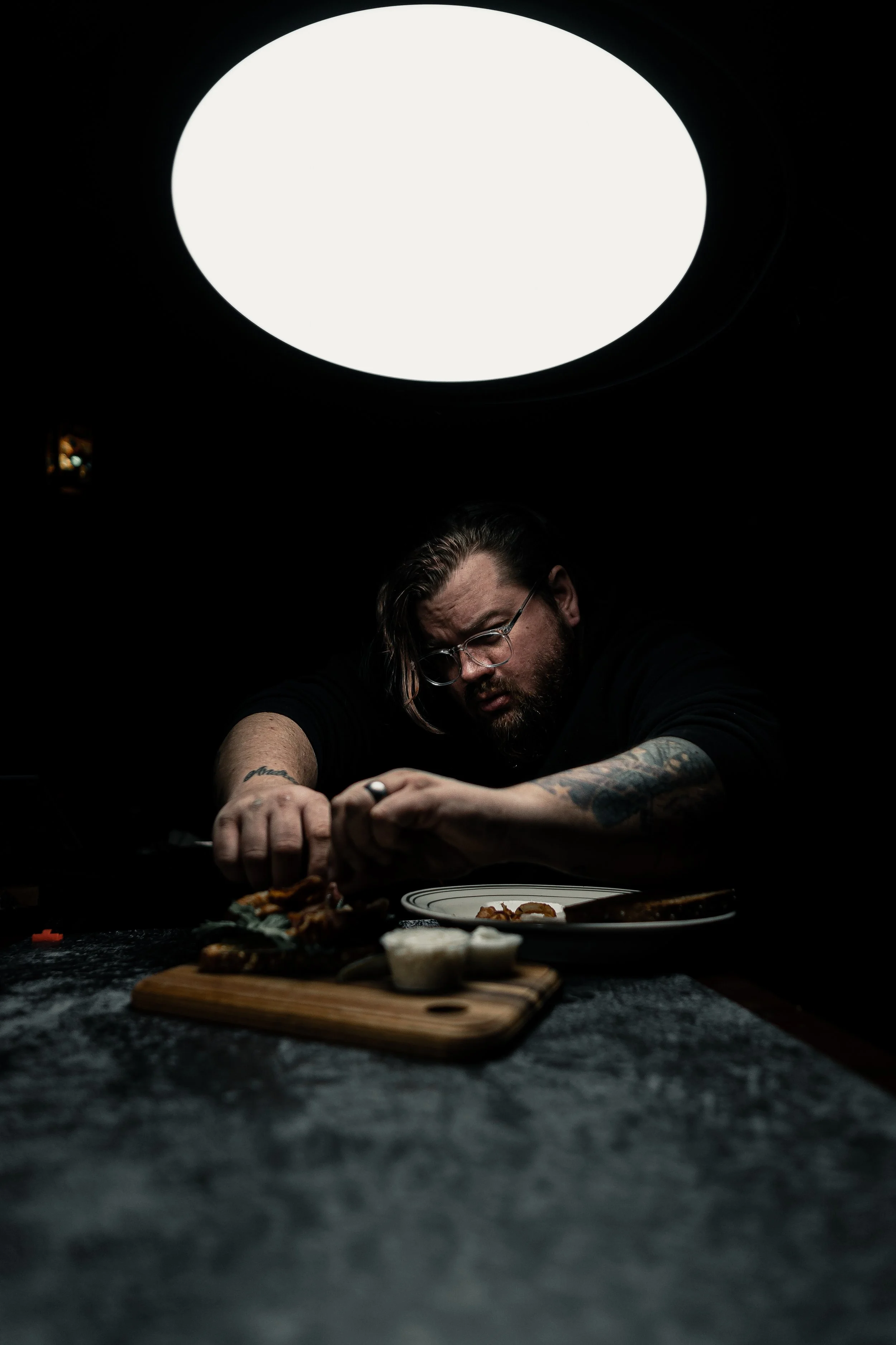 Food photographer assembling a plated dish during a studio shoot under controlled lighting.