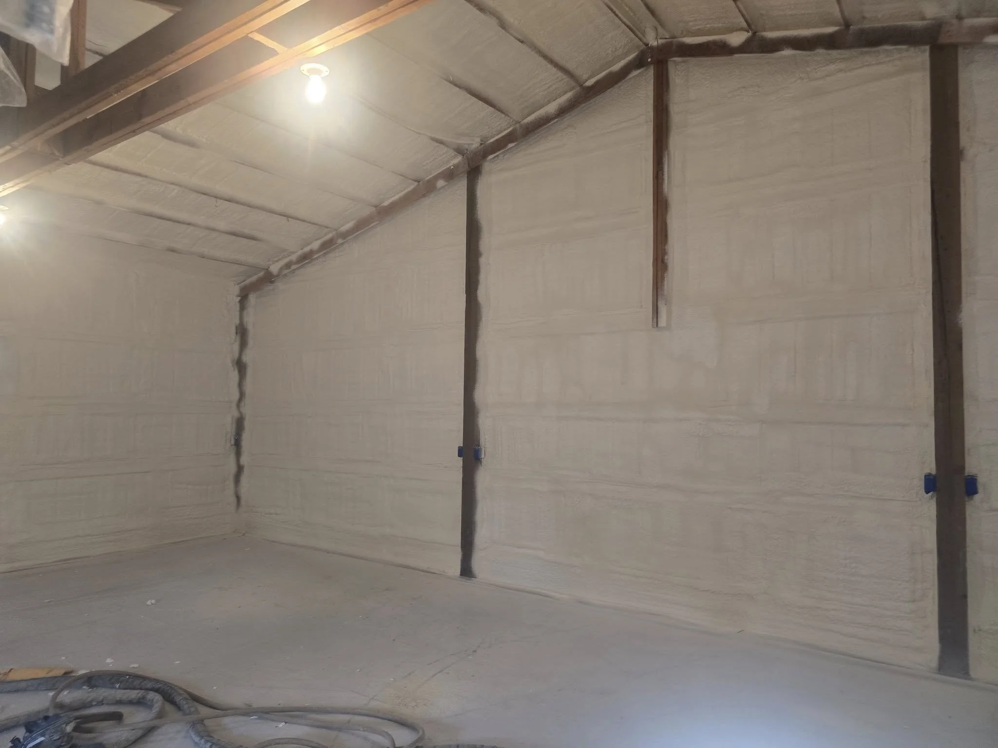 Interior of a room under construction with insulation on the walls and exposed wooden framing, with visible electrical wiring and support beams in the ceiling.