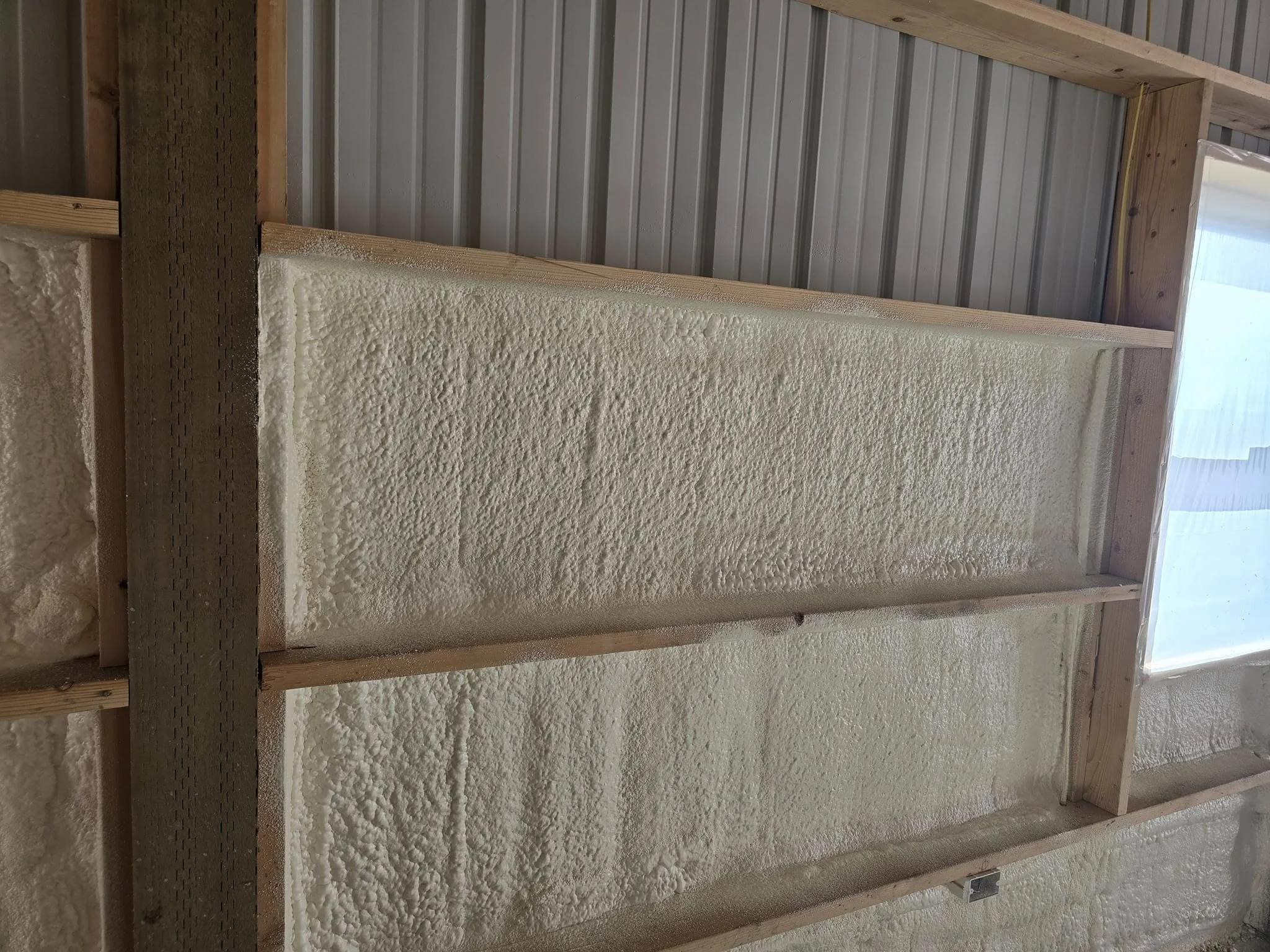 Close-up of foam spray insulation applied between wooden framing studs on a wall under construction.
