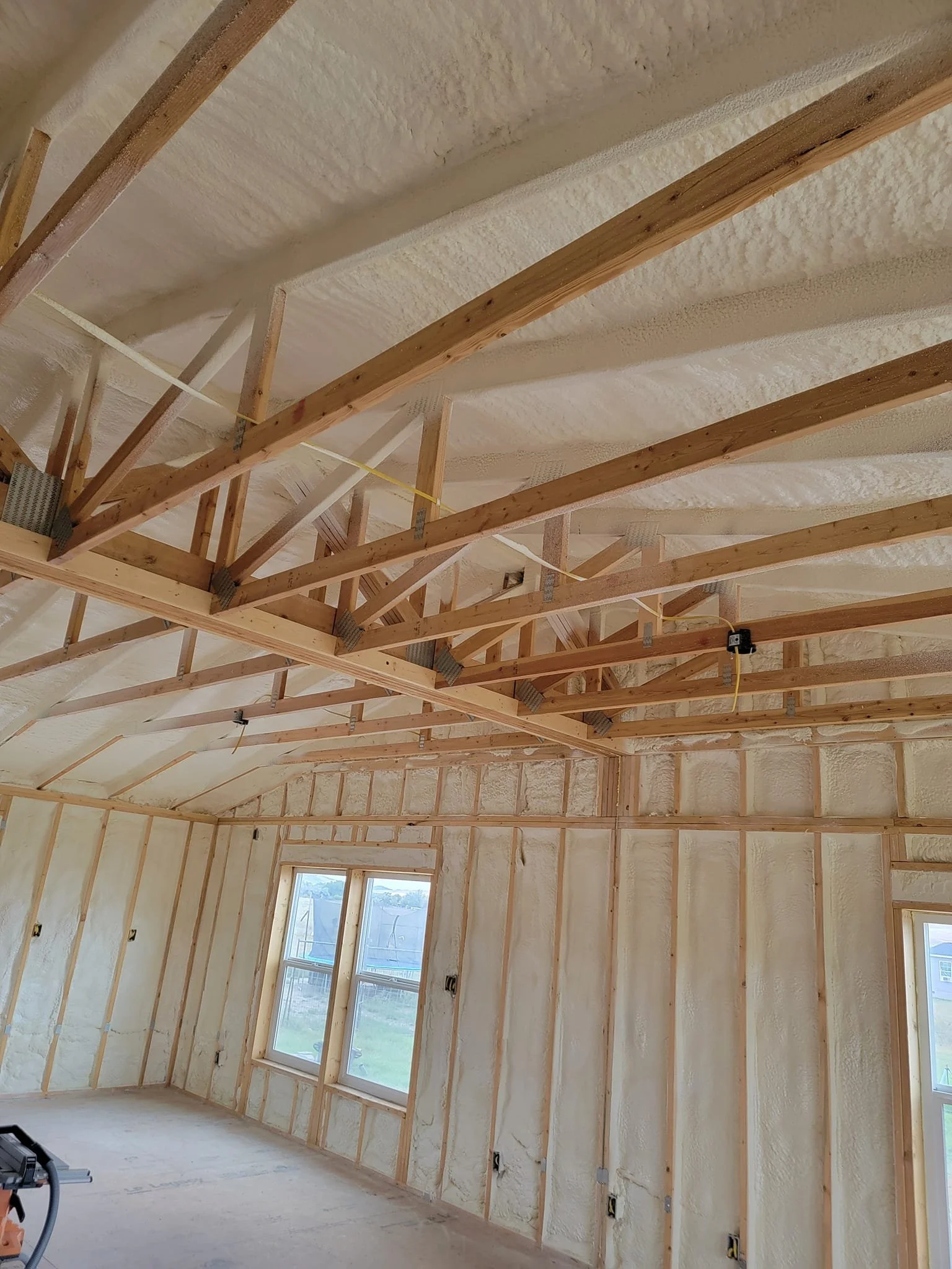 Interior of a house under construction with exposed wooden framing and spray foam insulation on the walls and ceiling.