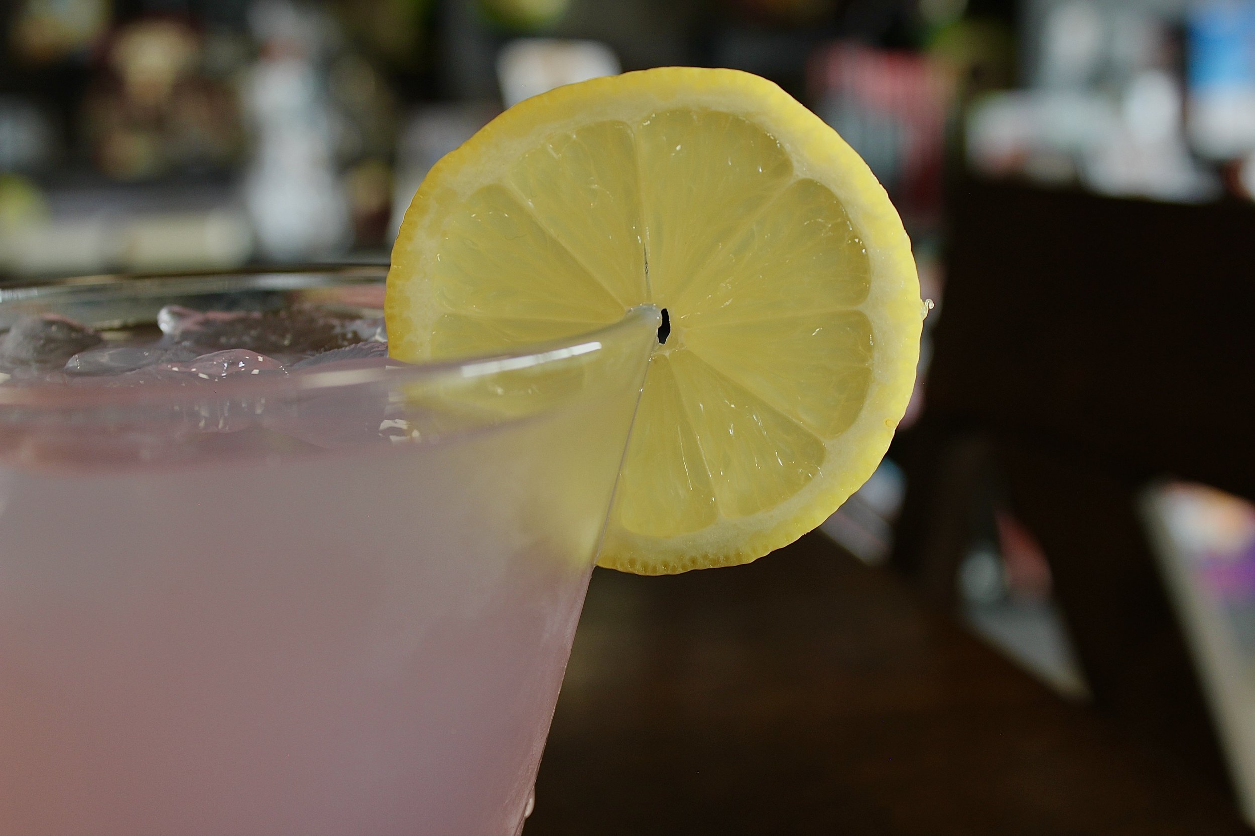 Close-up of a pink beverage with ice in a glass, garnished with a lemon slice on the rim.