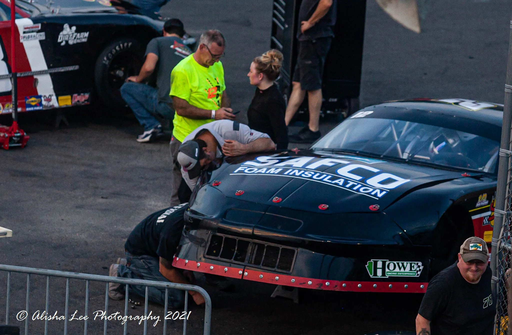 Race car with crew members working on it in the pit area of a racetrack.