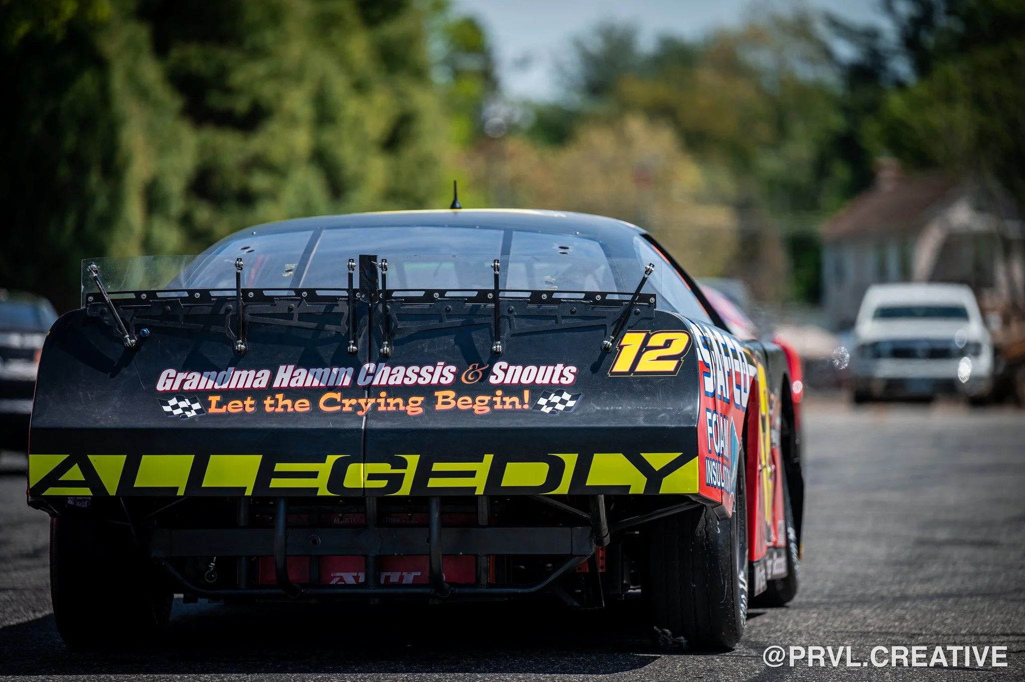 Race car with sponsorship and racing slogans on a road, background of trees and houses